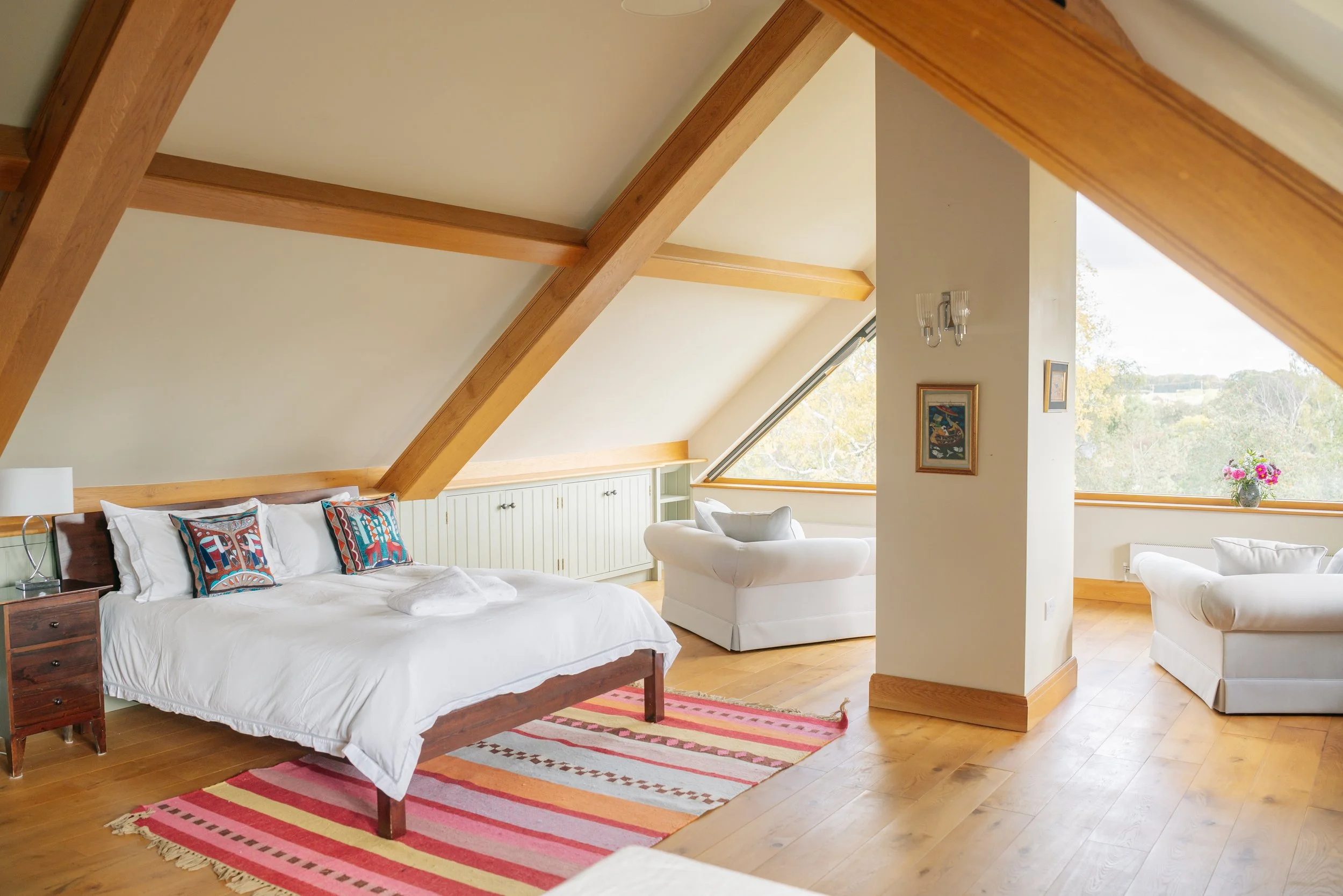 The Luxury Loft bedroom. It is spacious with vaulted ceilings, wooden beams, and large windows with views of the valley. The room has a bed, sitting area, and kitchenette.