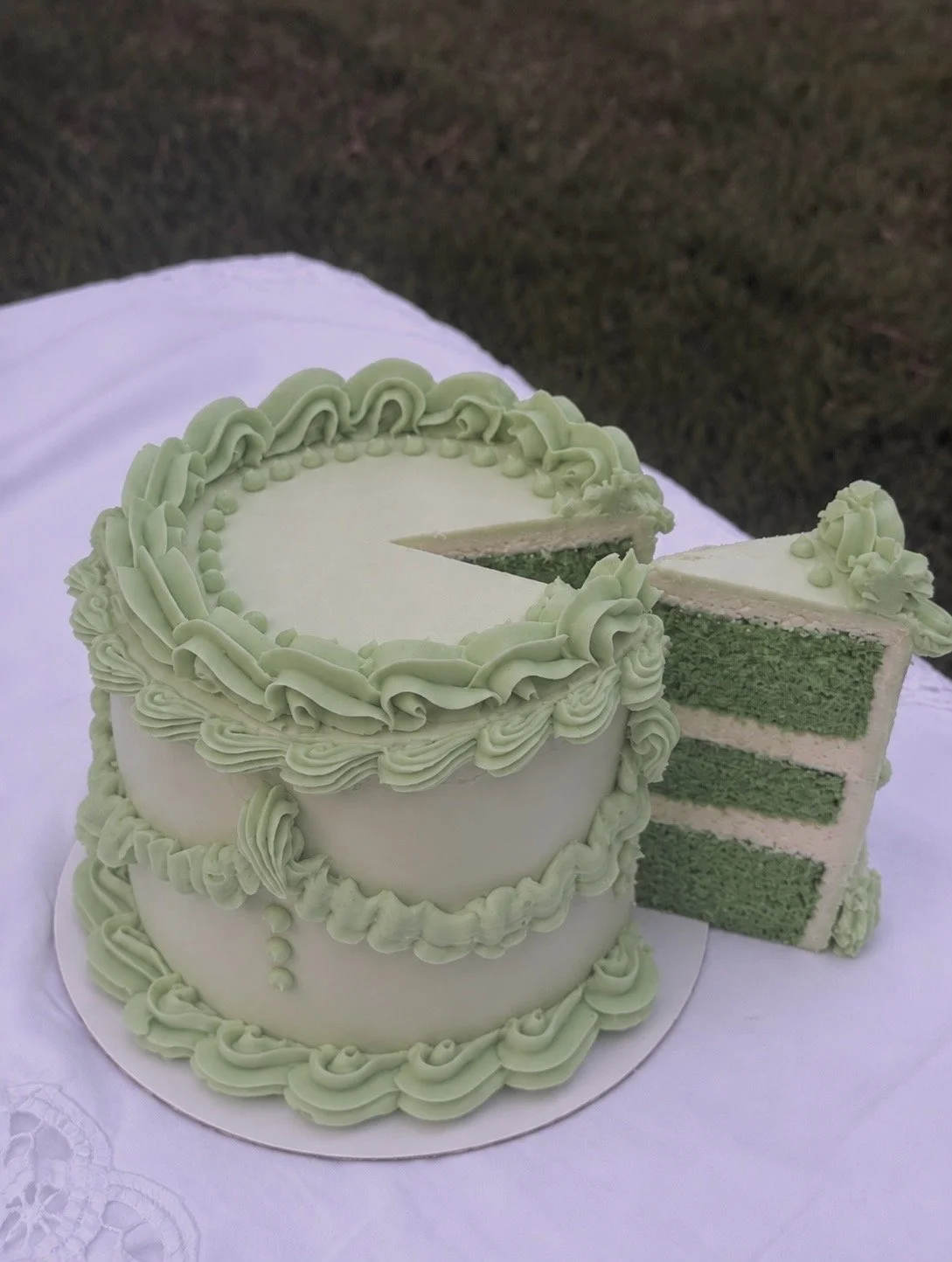 Three-layer pandan coconut cake with pale green Lambeth-style buttercream piping and a slice removed to show green cake layers and coconut filling.