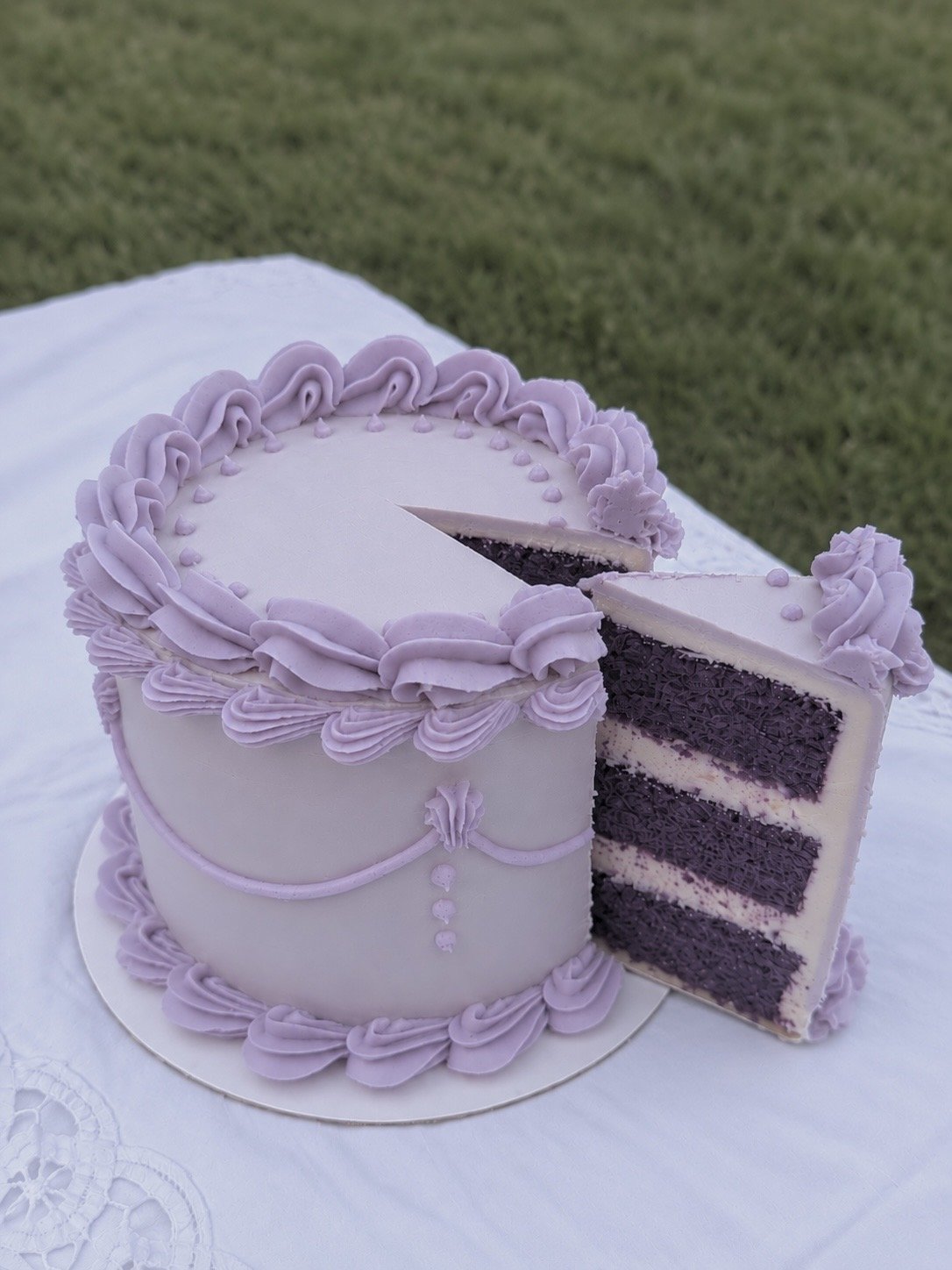 Close-up of a sliced ube cake showing purple sponge layers, pale cream filling, and lavender buttercream decoration.