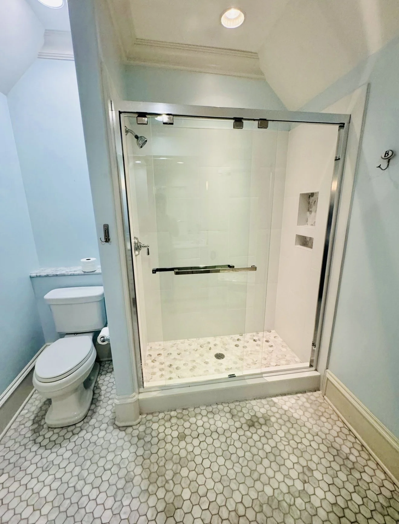 A bathroom with a glass-enclosed shower, a toilet, and beige hexagon tiles on the floor.