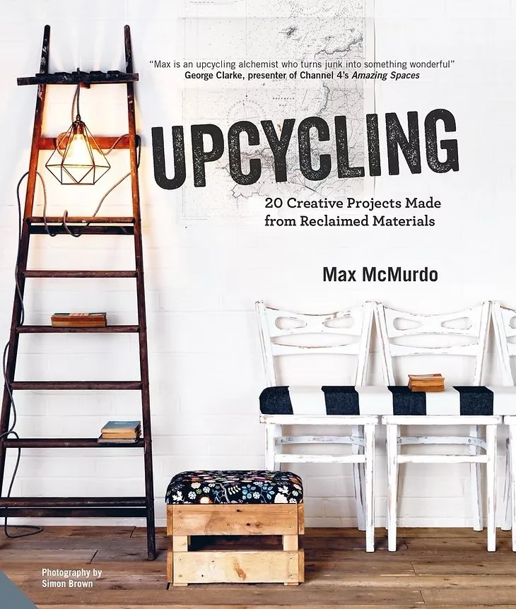 Book cover titled 'Upcycling: 20 Creative Projects Made from Reclaimed Materials' by Max McMurdo, featuring a decorative hanging lamp on a ladder, two white chairs with black cushions, and a wooden box with cushions, against a white wall with a quote from George Clarke.
