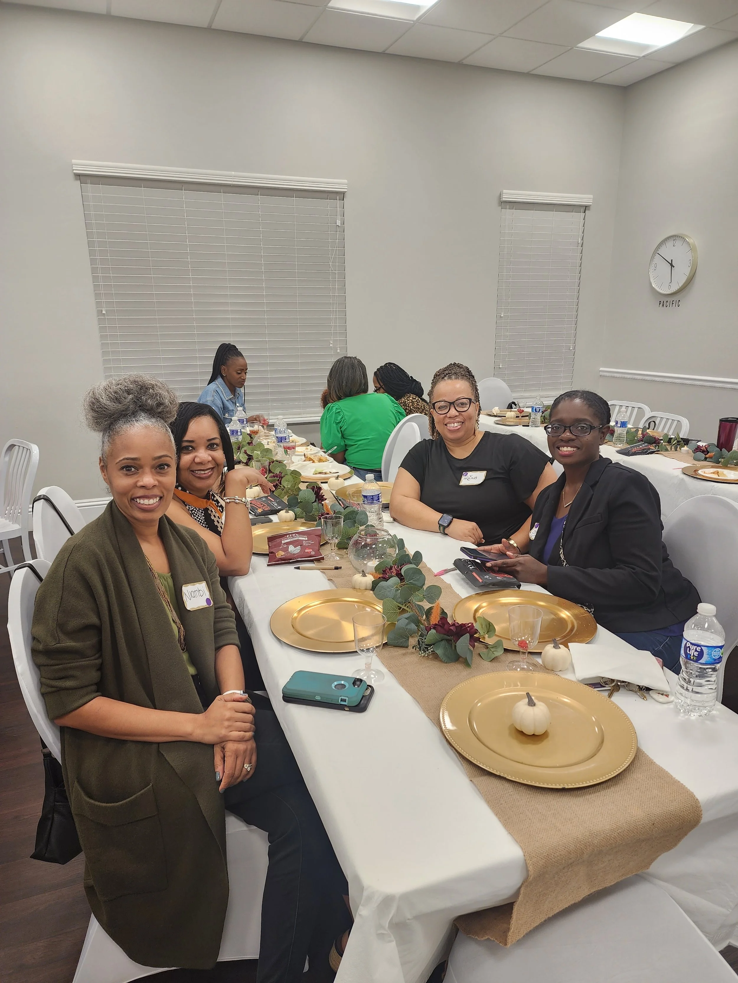 Group of women sitting around a decorated banquet table at an indoor event, smiling at the camera.