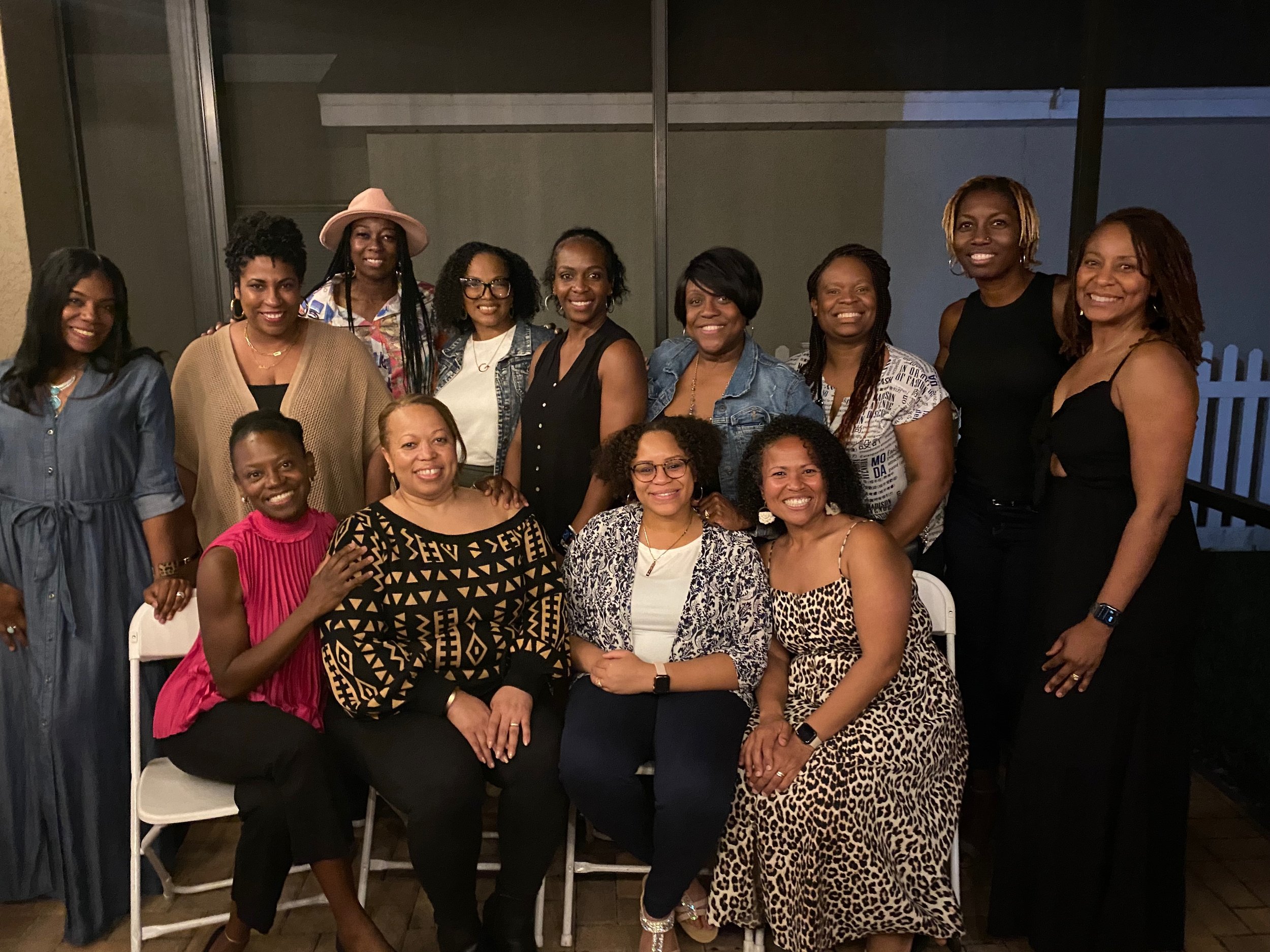 Group of eleven women gathered for a photo indoors, some sitting and others standing, smiling at the camera.