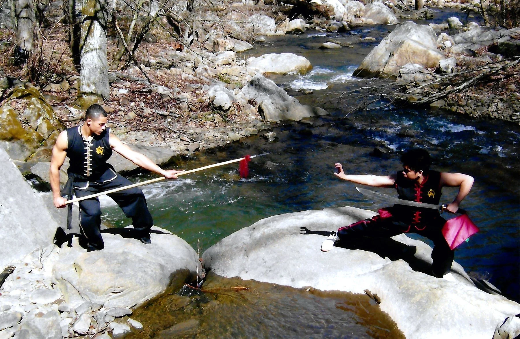 James Whitley III with a spear facing a training partner with a broadsword beside a mountain creek