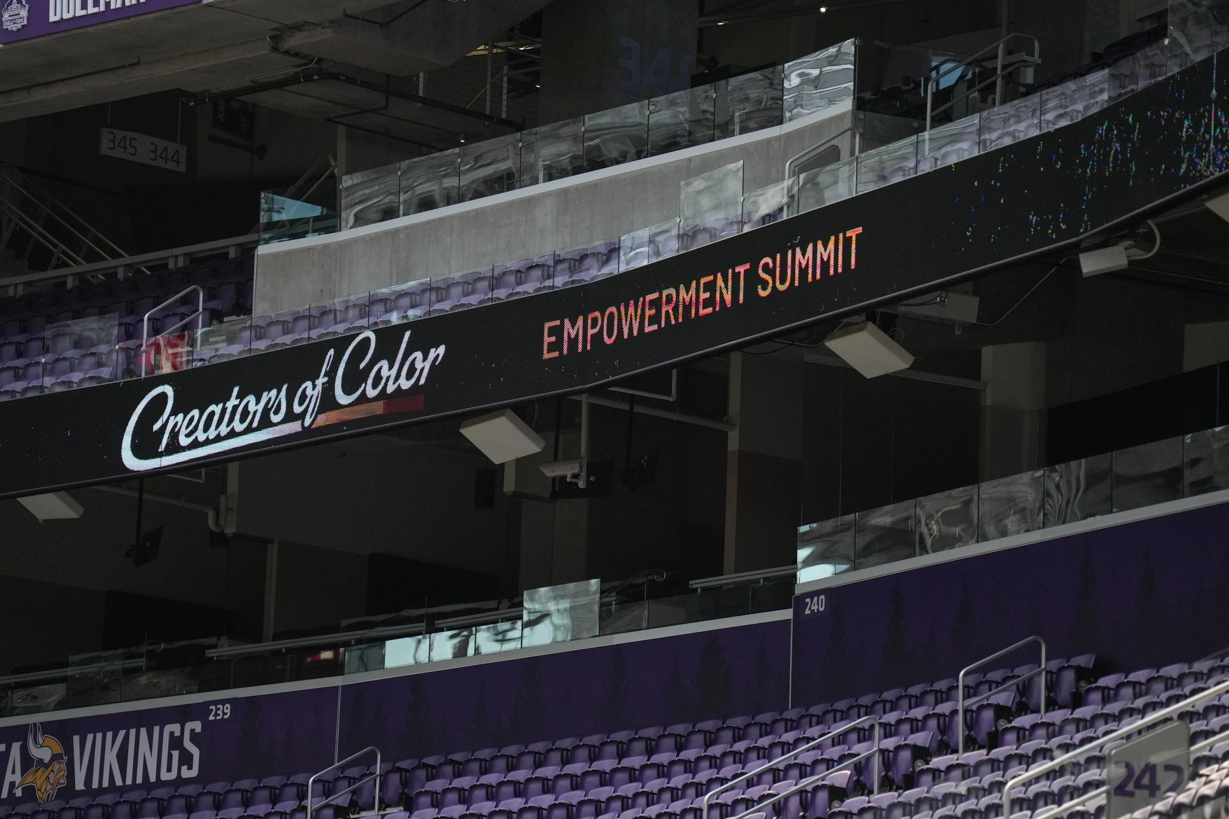 Digital display board showing event name 'Creators of Color' and subtitle 'Empowerment Summit', inside a stadium with purple seats and a Vikings logo.