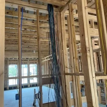Interior of a new home under construction with exposed wood framing, electrical wires, plumbing, and unfinished rooms.
