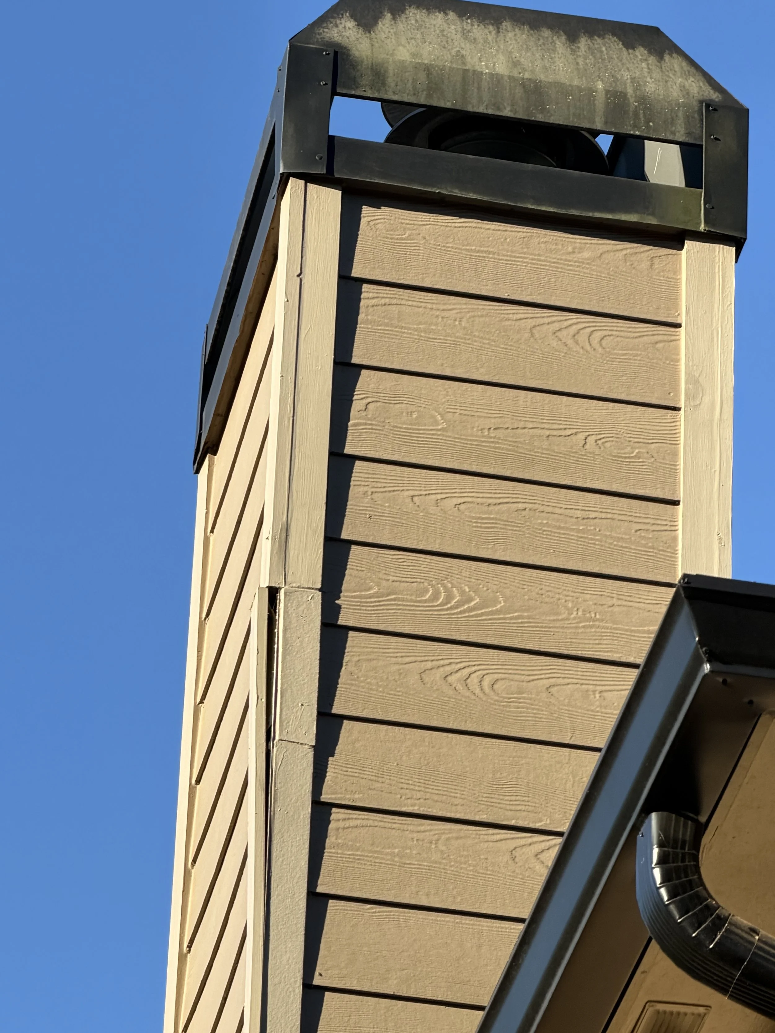 Close-up of a rooftop turbine vent on a wood-sided building against a clear blue sky