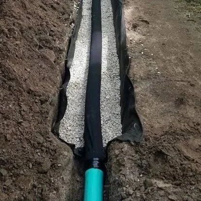 Black perforated drainage pipe laid in a gravel-filled trench with a green outlet pipe.