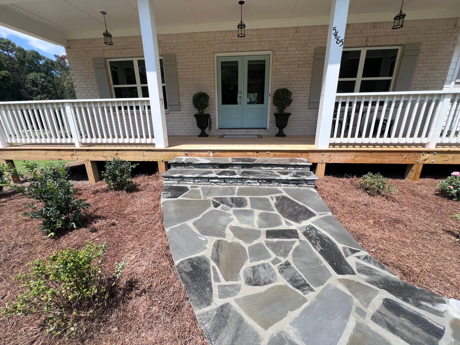 Front porch with teal double doors, white railings, black planters, and a flagstone walkway