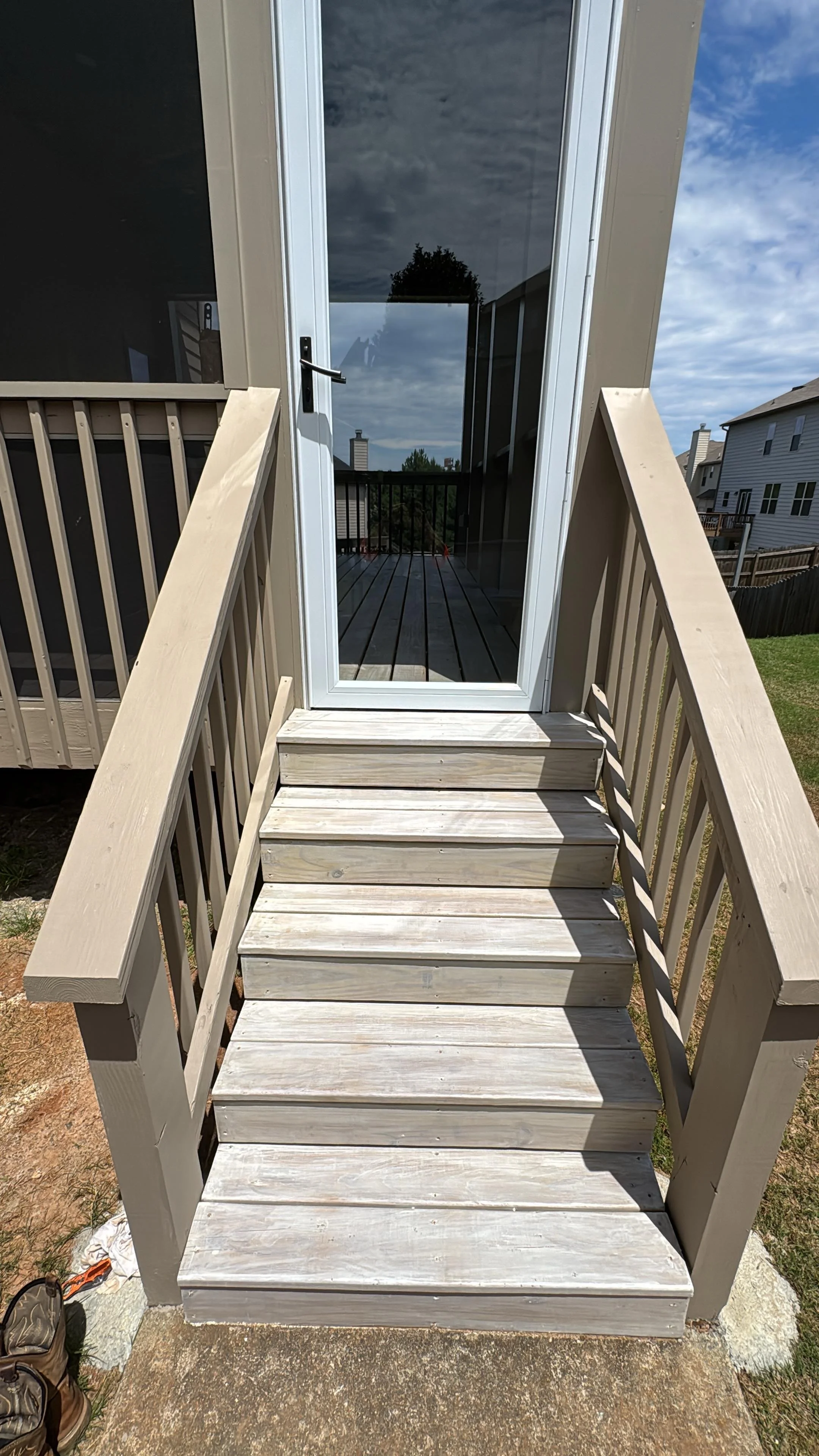 Wooden outdoor staircase with beige railings leading to a glass-paneled back door and elevated deck.