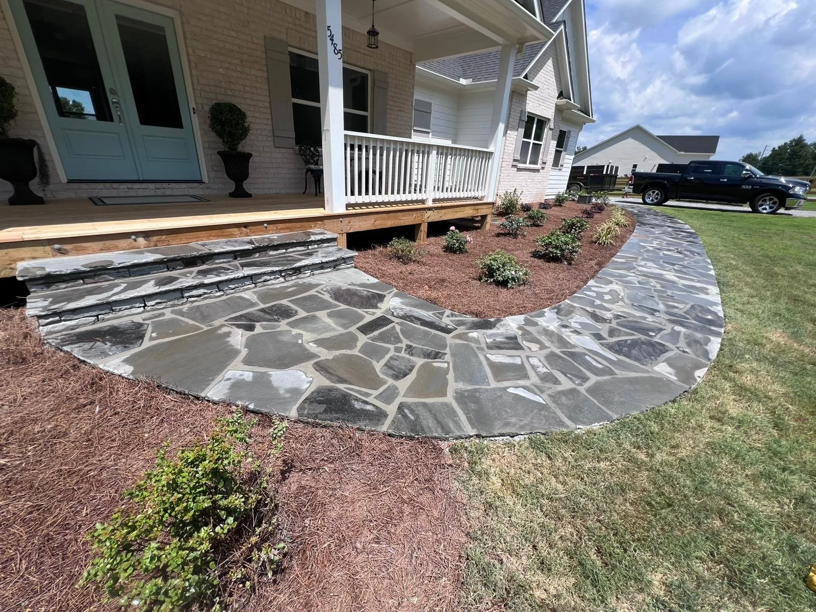 Front porch with white railing, stone steps, curved flagstone walkway, and landscaped garden beds
