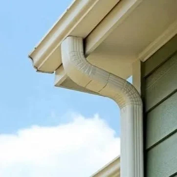 White vinyl rain gutter and downspout attached to a house under a blue sky
