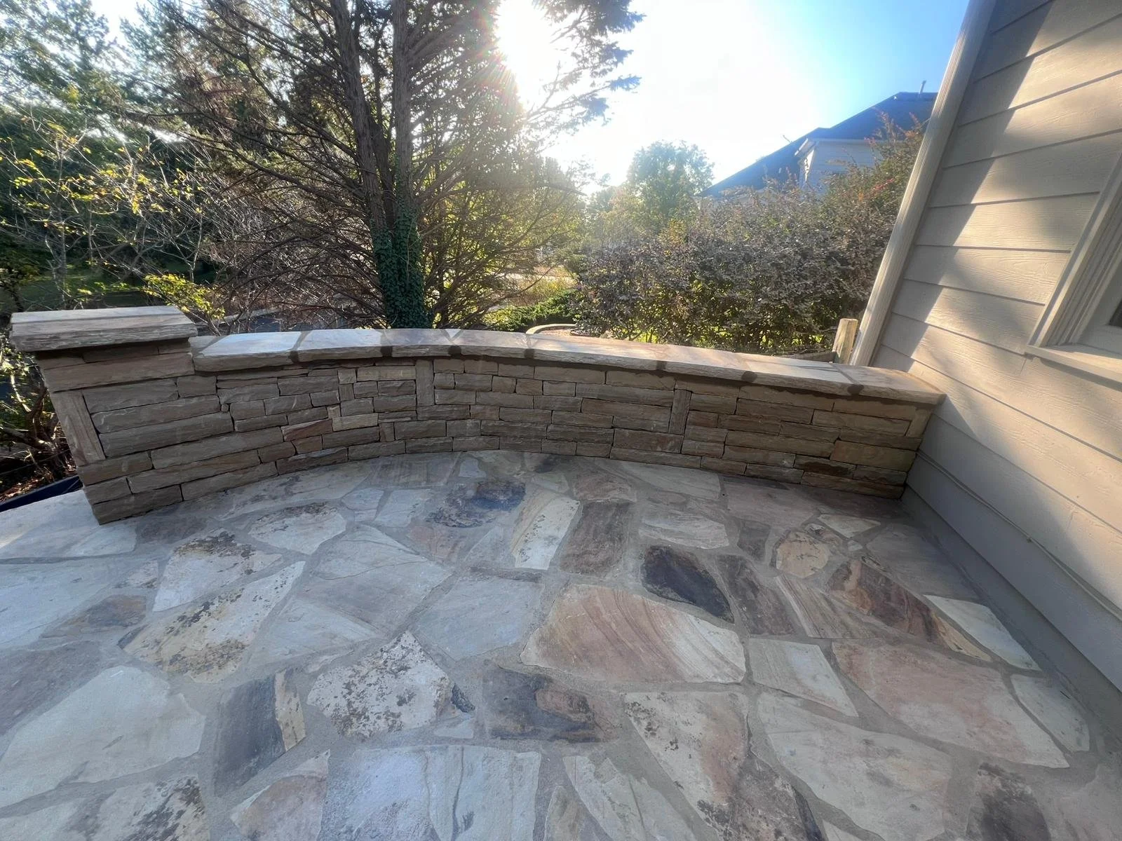 Stone-paved patio with a curved stacked-stone retaining wall beside a house and landscaped yard