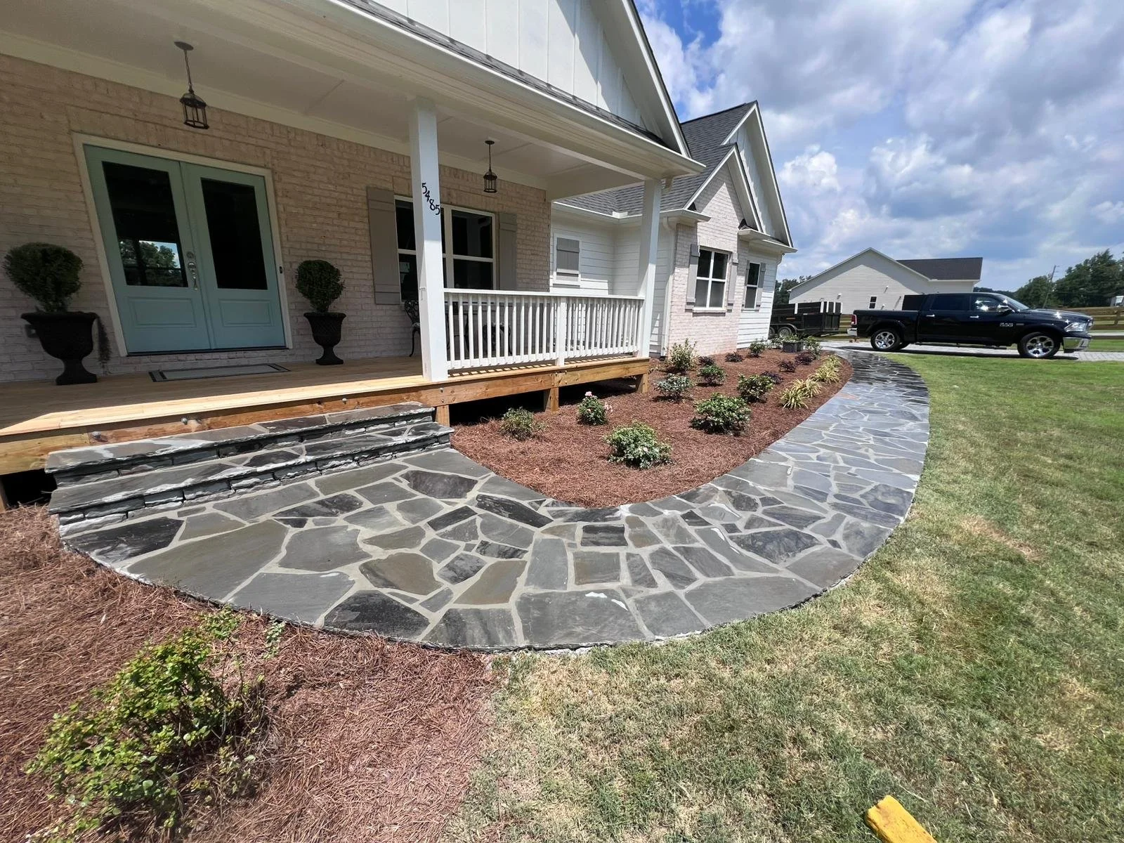 Landscaped front entrance with covered porch, white brick house, curved flagstone walkway, and black pickup truck