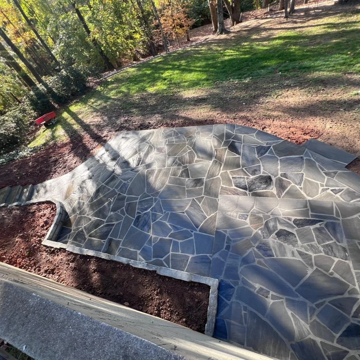 Irregular flagstone patio beside a wooded lawn and garden beds