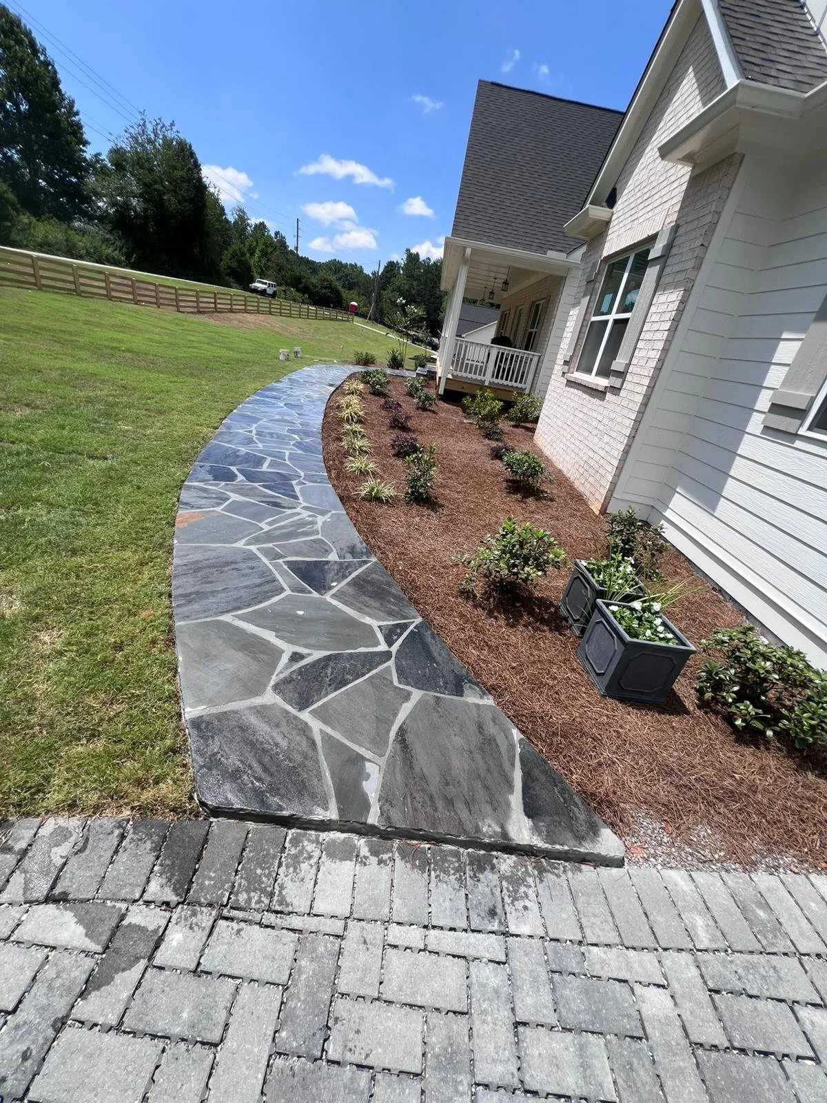 Flagstone walkway beside a landscaped flower bed leading to the porch of a white brick house