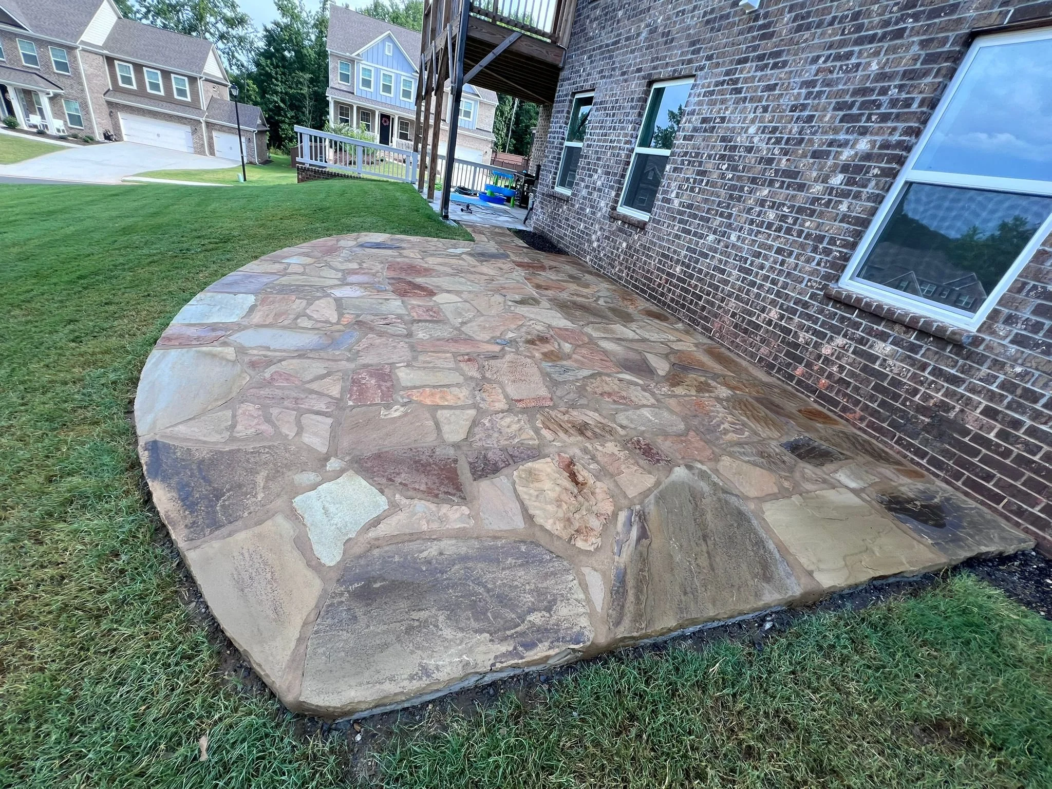 Flagstone patio beside a brick house with neighboring suburban homes and lawns