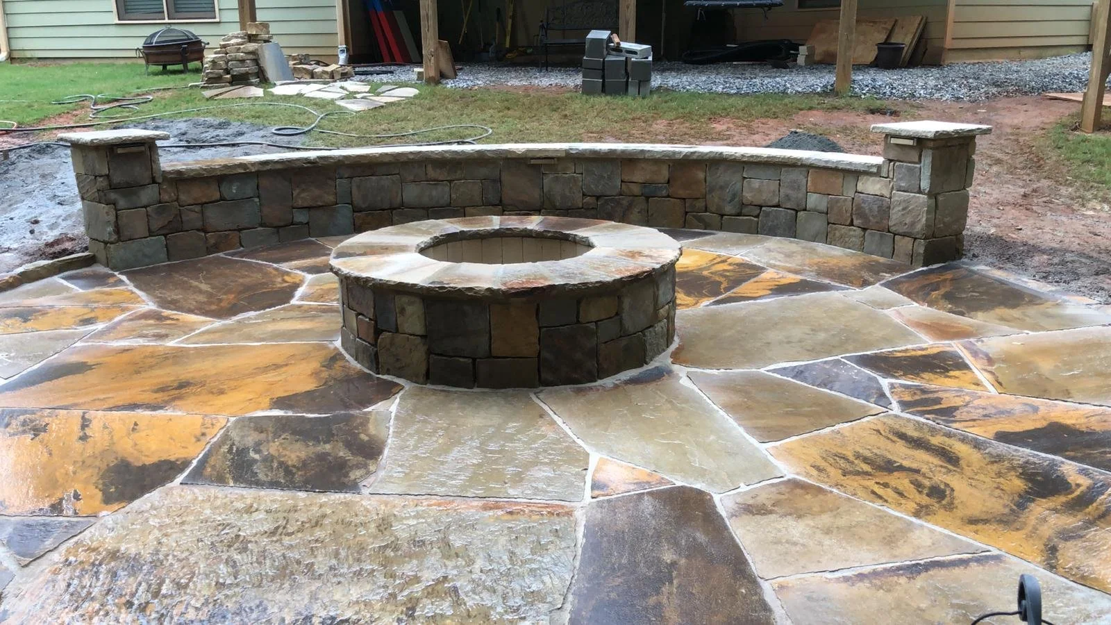 Stone outdoor fire pit surrounded by a curved retaining wall and natural flagstone patio