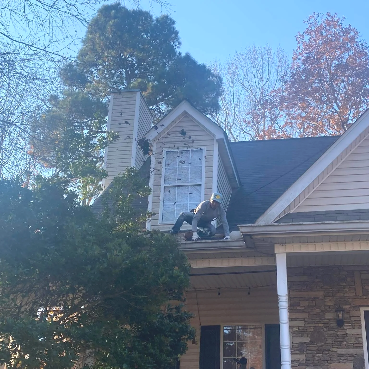 Worker crouching on the roof of a suburban house near a dormer window