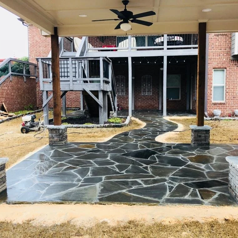 Covered brick patio with a ceiling fan, wooden posts, raised deck, and irregular slate stone walkway