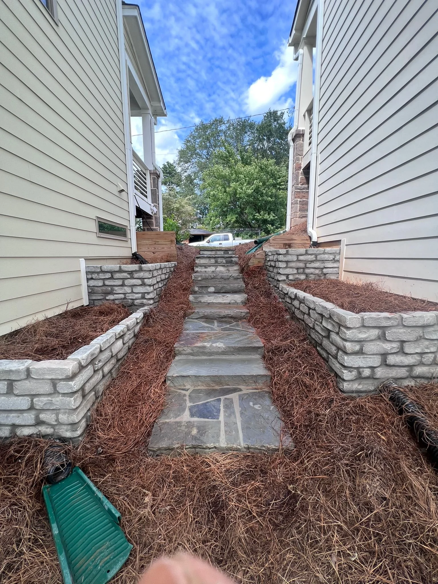 Stone steps between two-sided houses, bordered by stacked-stone retaining walls and pine straw landscaping.
