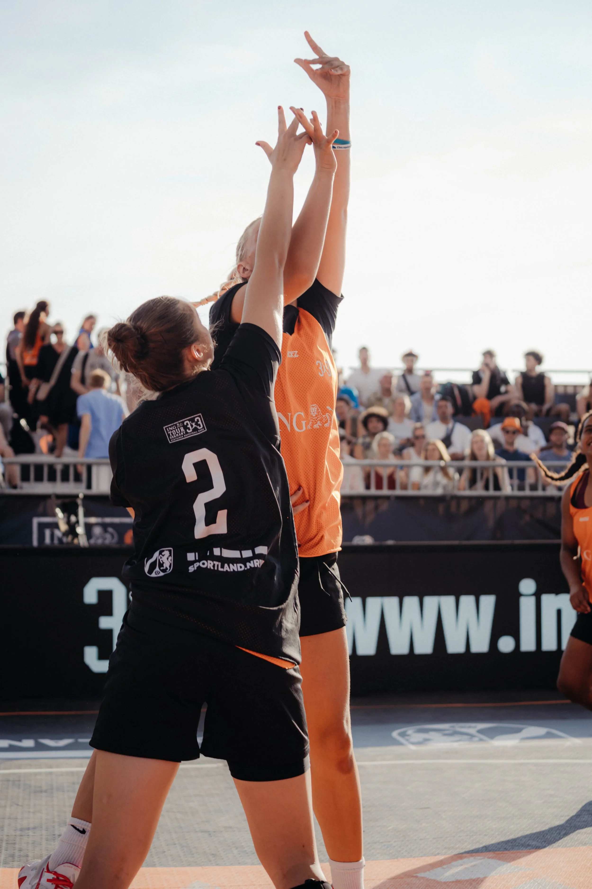 Two female basketball player, one going up for a layup, while the other one is guarding her