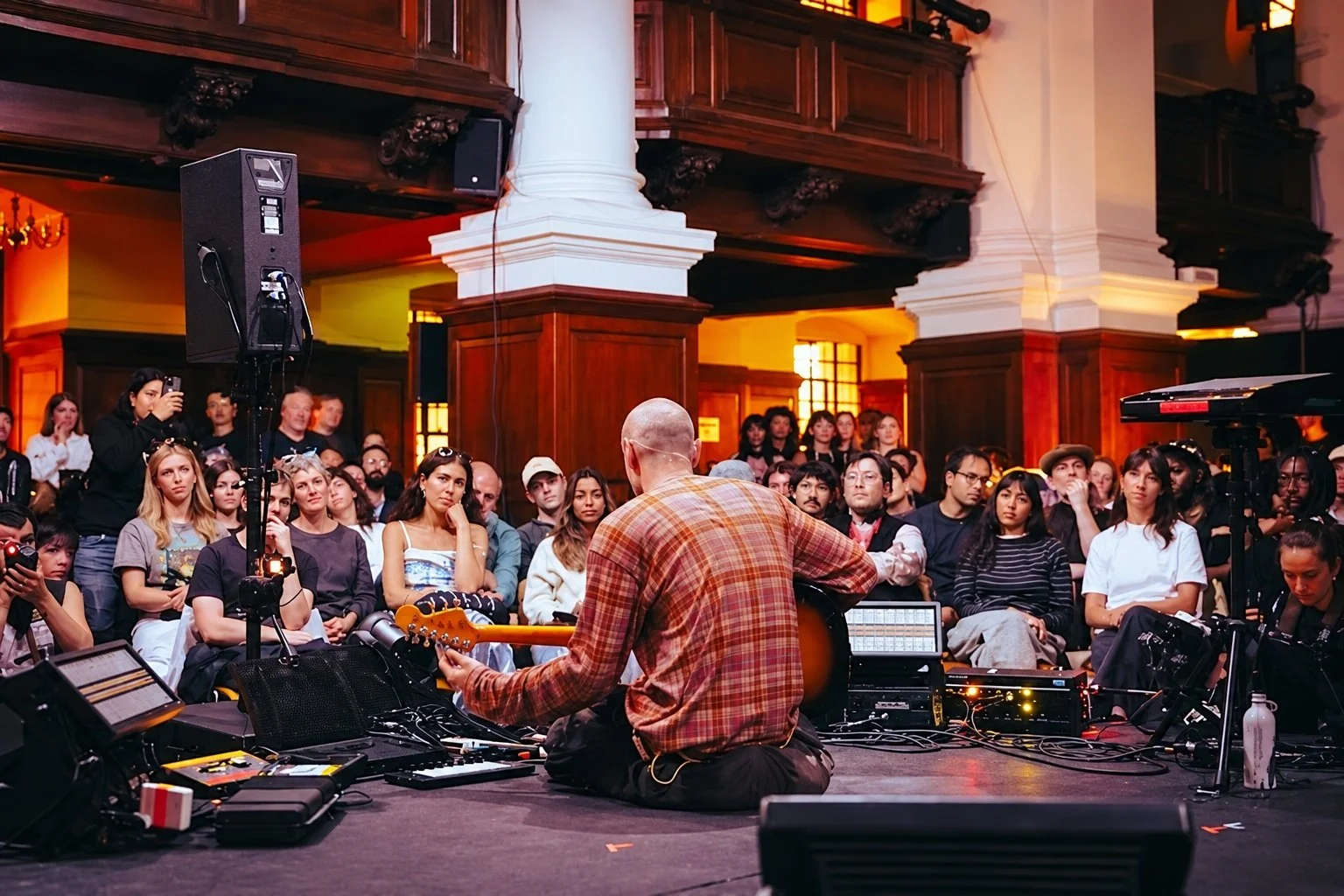 Seated guitarist performing to an intimate audience.