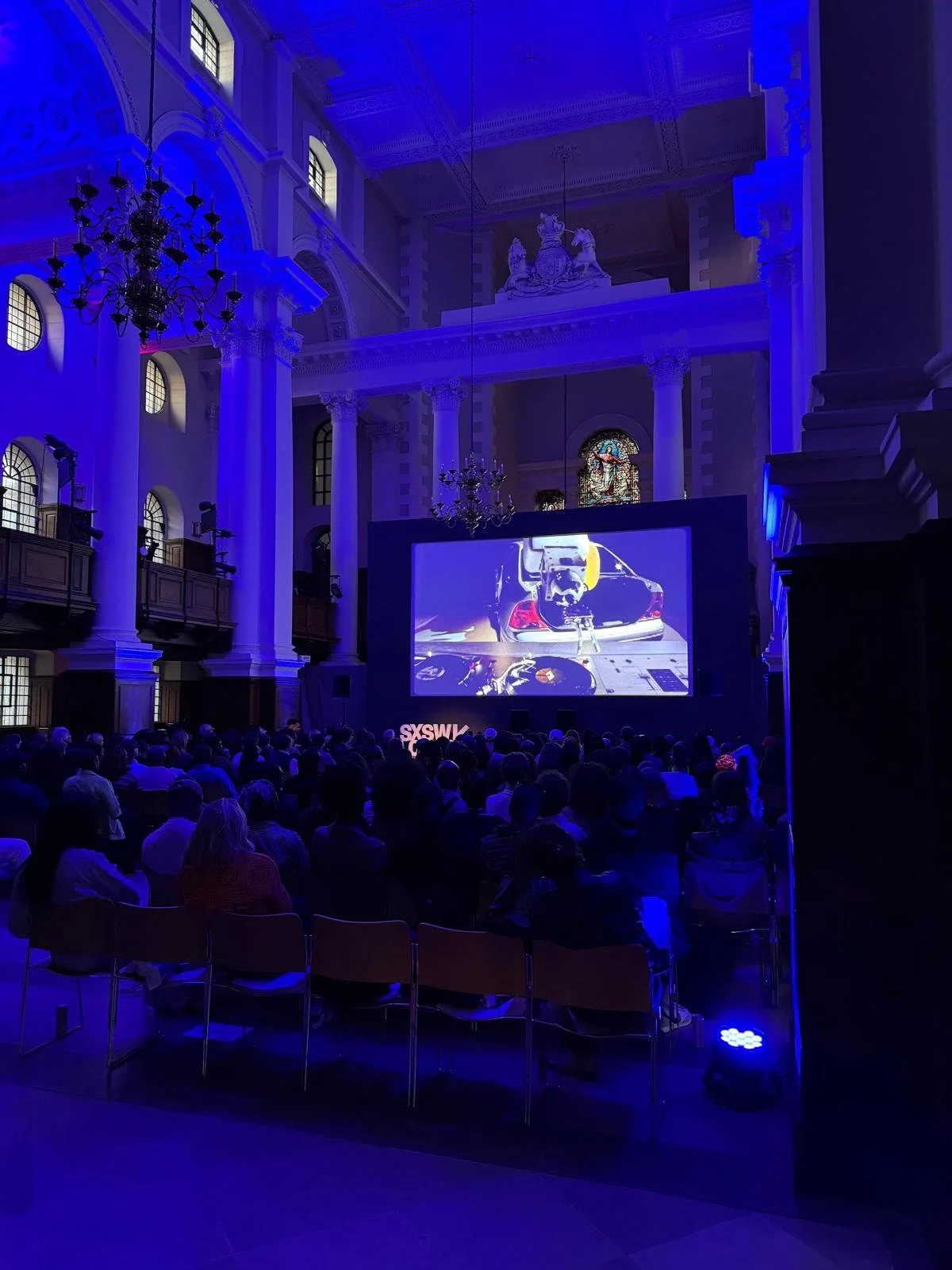 Audience watching a large screen in the Nave beneath blue and purple event lighting