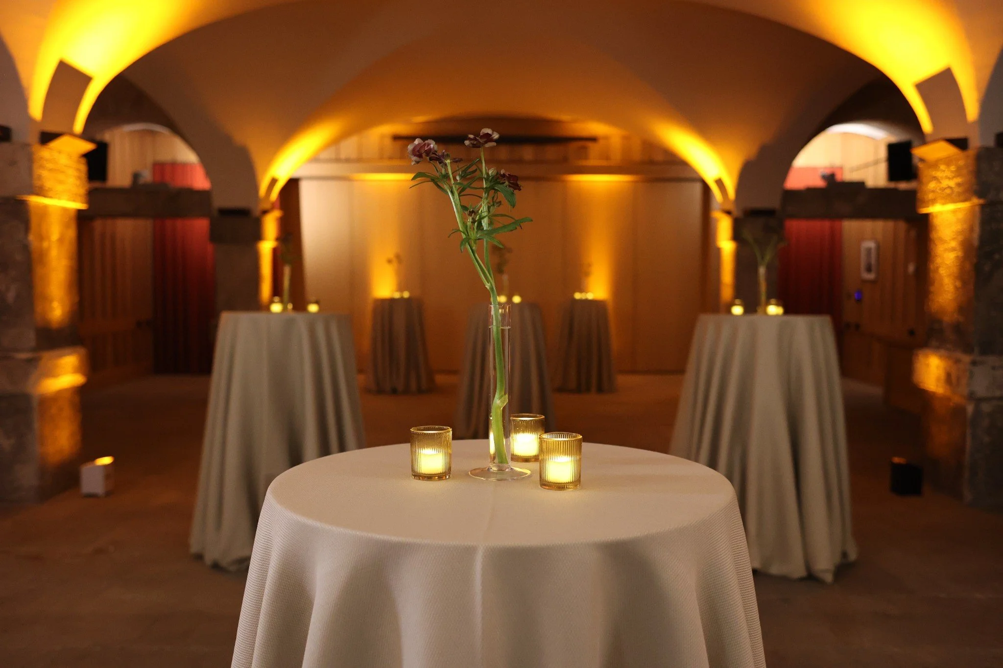Candlelit poseur tables beneath the Crypt’s vaulted ceiling with amber event lighting.