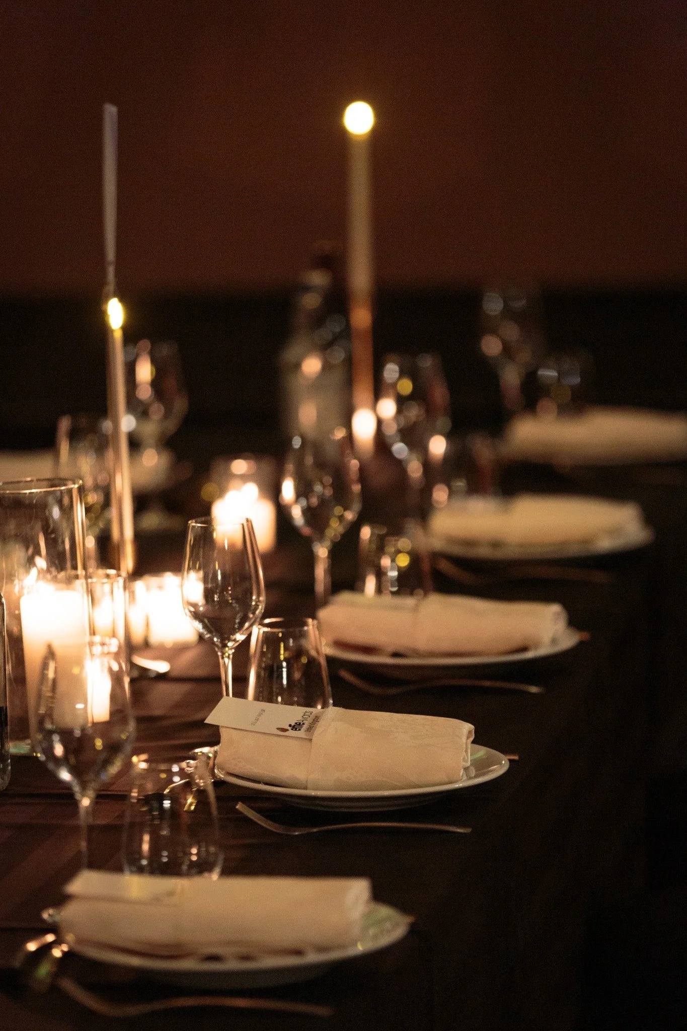 Close-up of candlelight, glassware and place settings at a dinner.