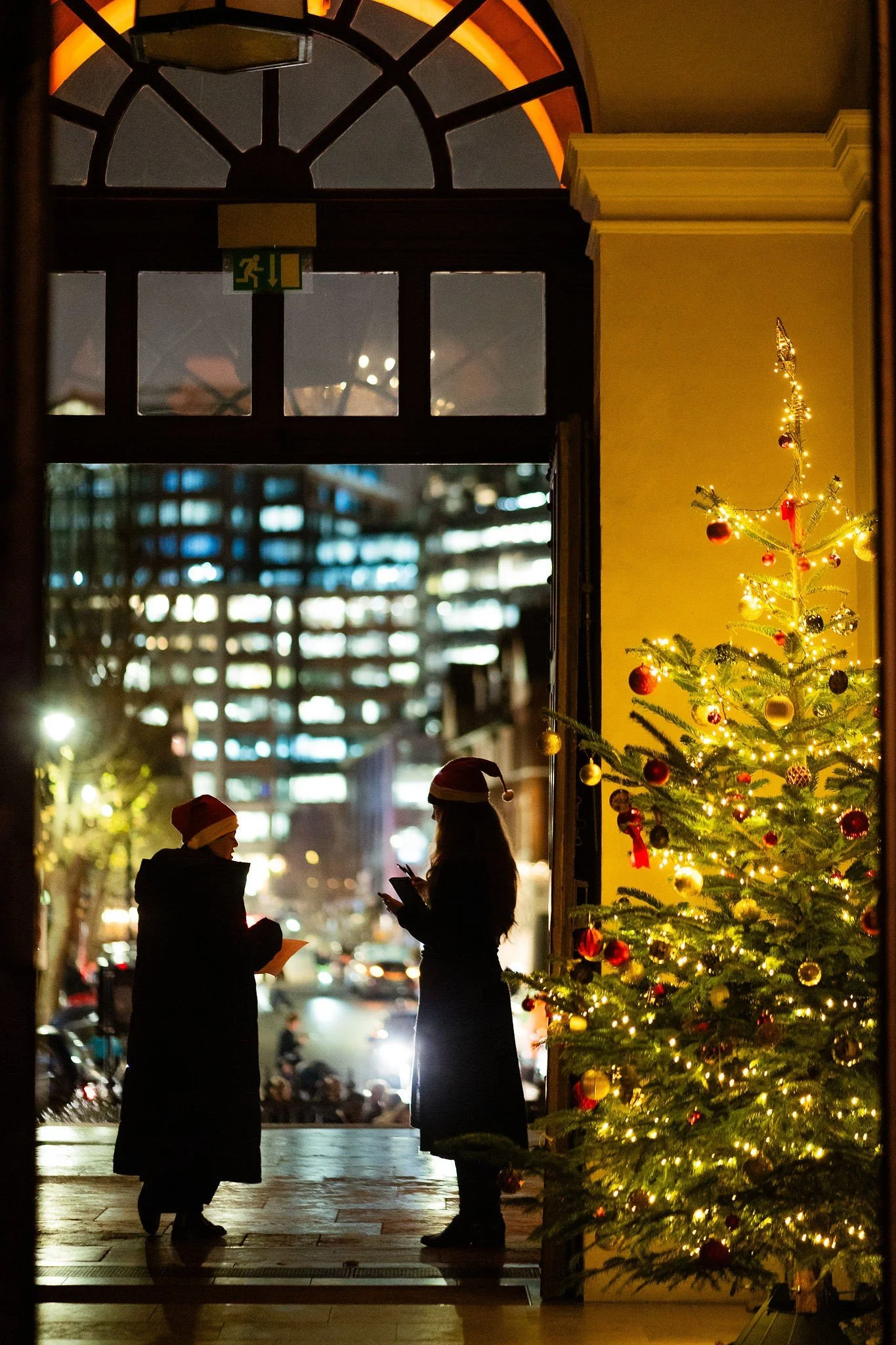 Guests arriving through a candlelit doorway beside a Christmas tree.