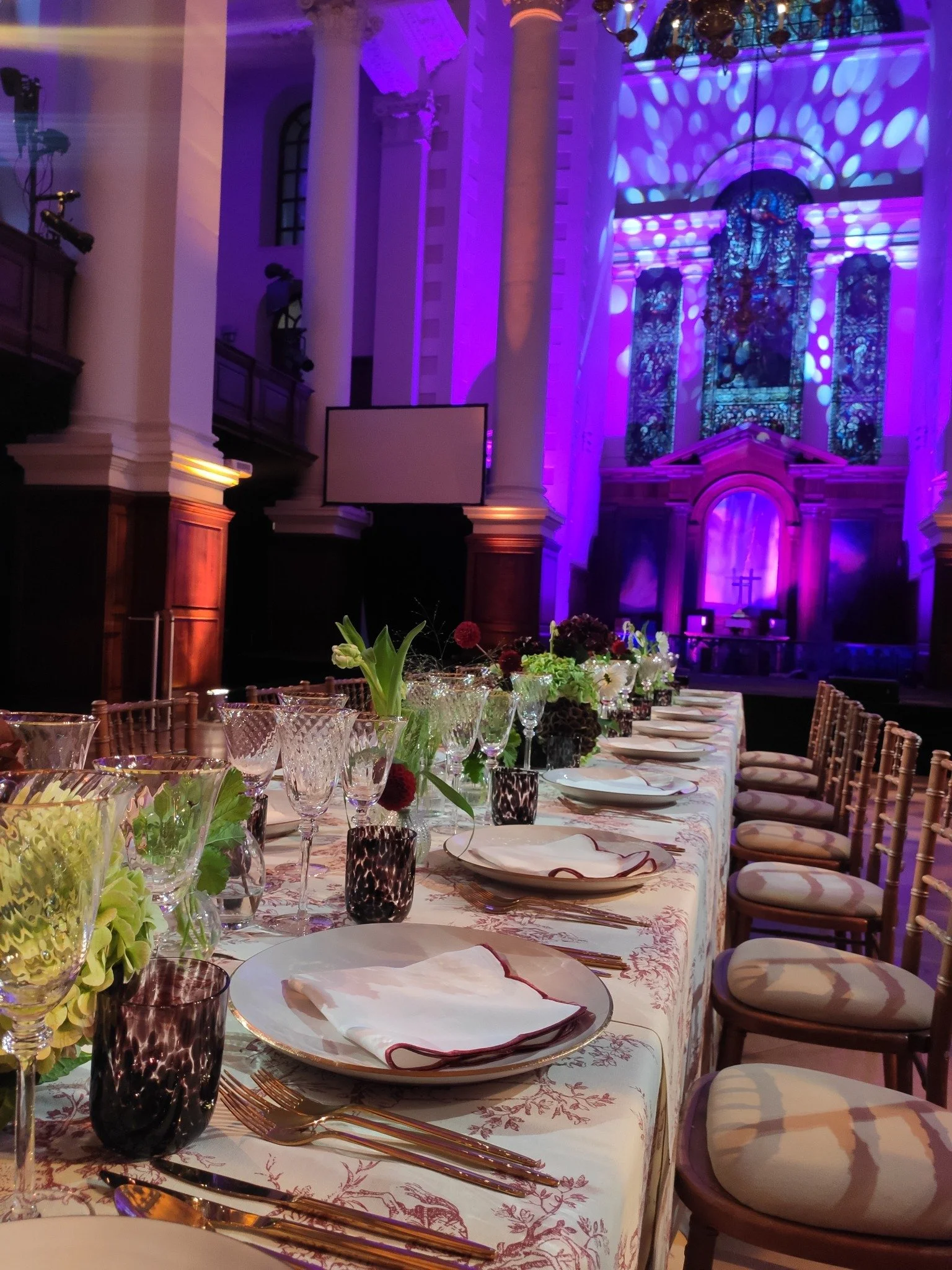 Dinner table laid with glassware and floral arrangements in the Nave under purple event lighting