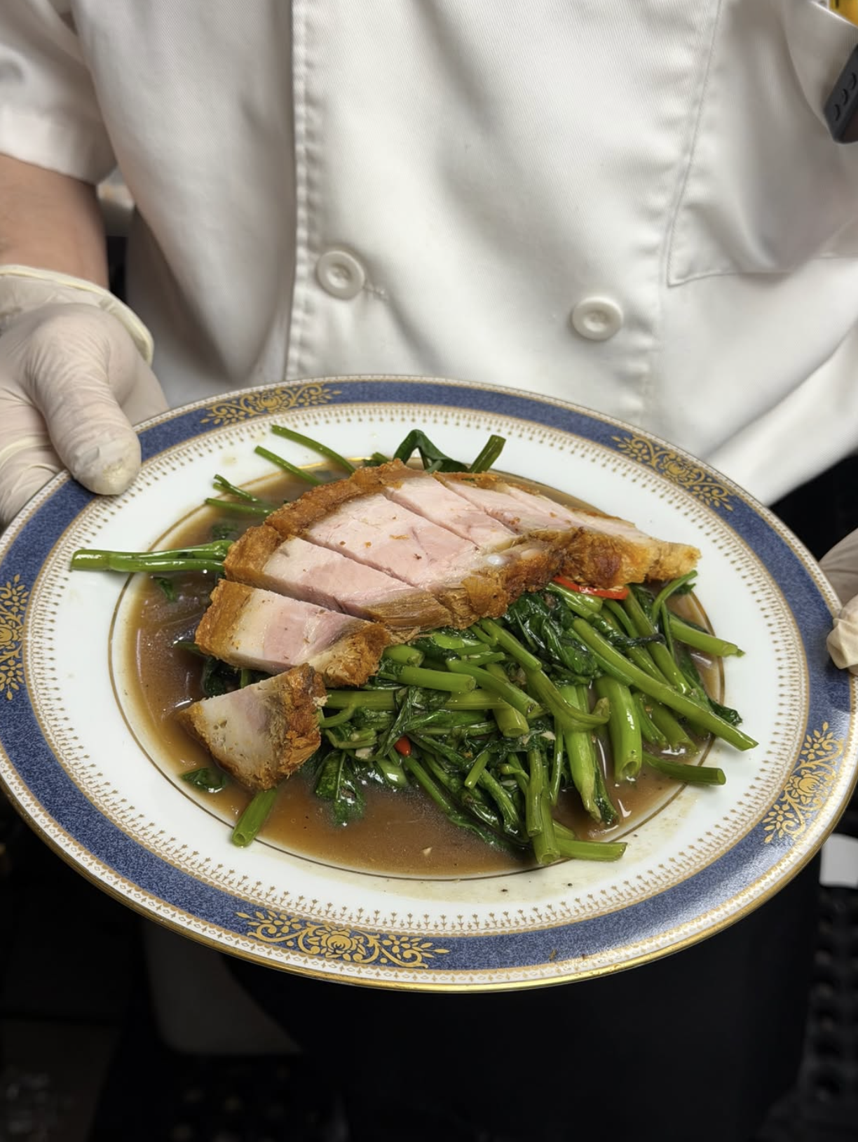 Chef holding a decorative plate of crispy pork belly with dark soy sauce, served over sautéed green water spinach.