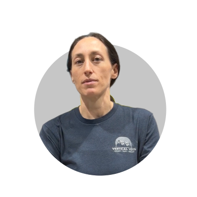 Woman with dark hair wearing a navy blue t-shirt with a logo, posing against a gray circular background.