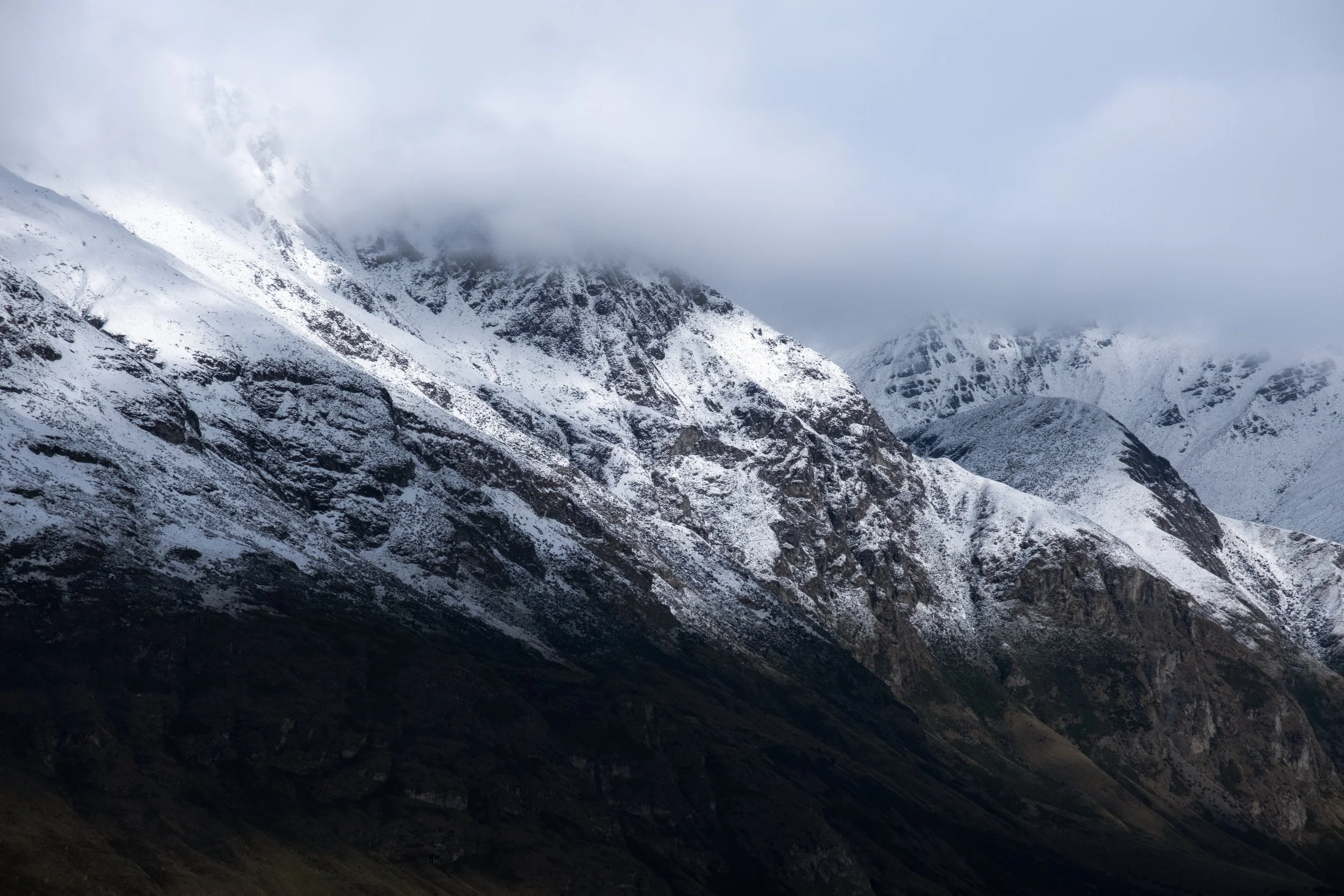 Snow-covered mountain range with clouds obscuring the peaks, dark rocky slopes.
