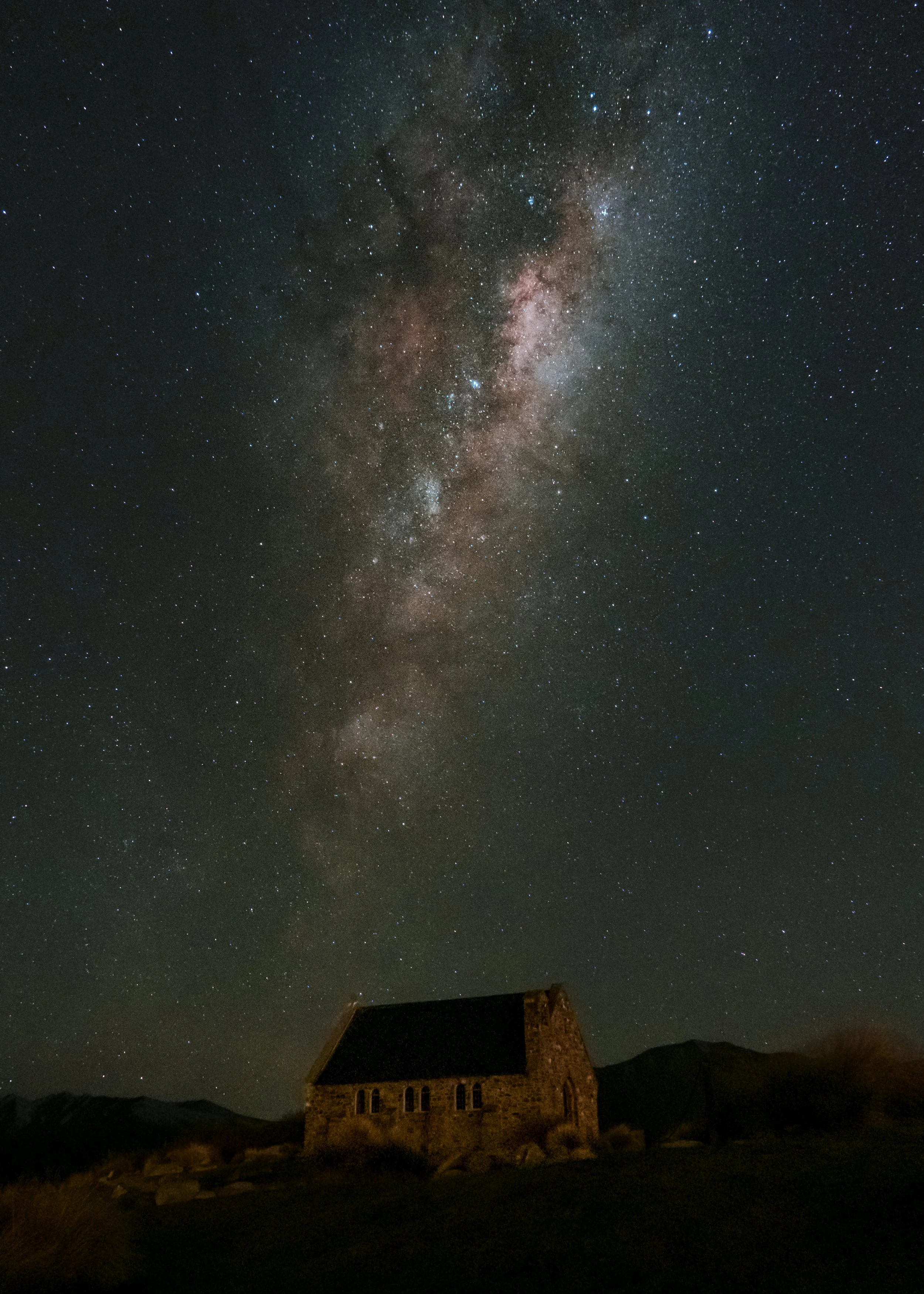 Night sky filled with stars and the Milky Way galaxy over a house in a rural area.