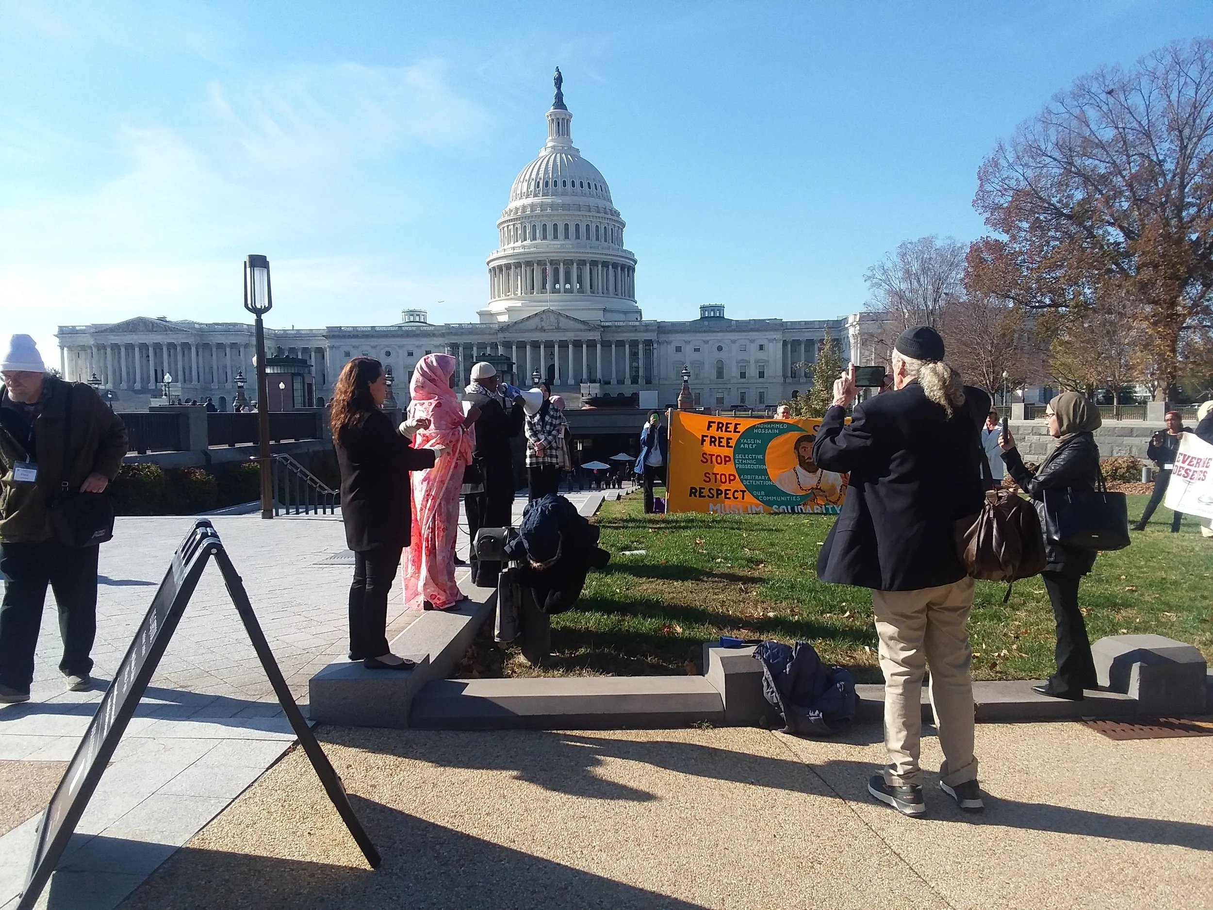 Members of the Coalition for Civil Freedoms gather outside the U.S. Capitol building in Washington, D.C., holding signs and a megaphone.