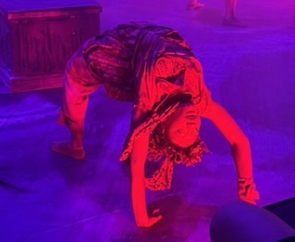 Person in colorful lighting performing a backbend yoga pose on the floor.