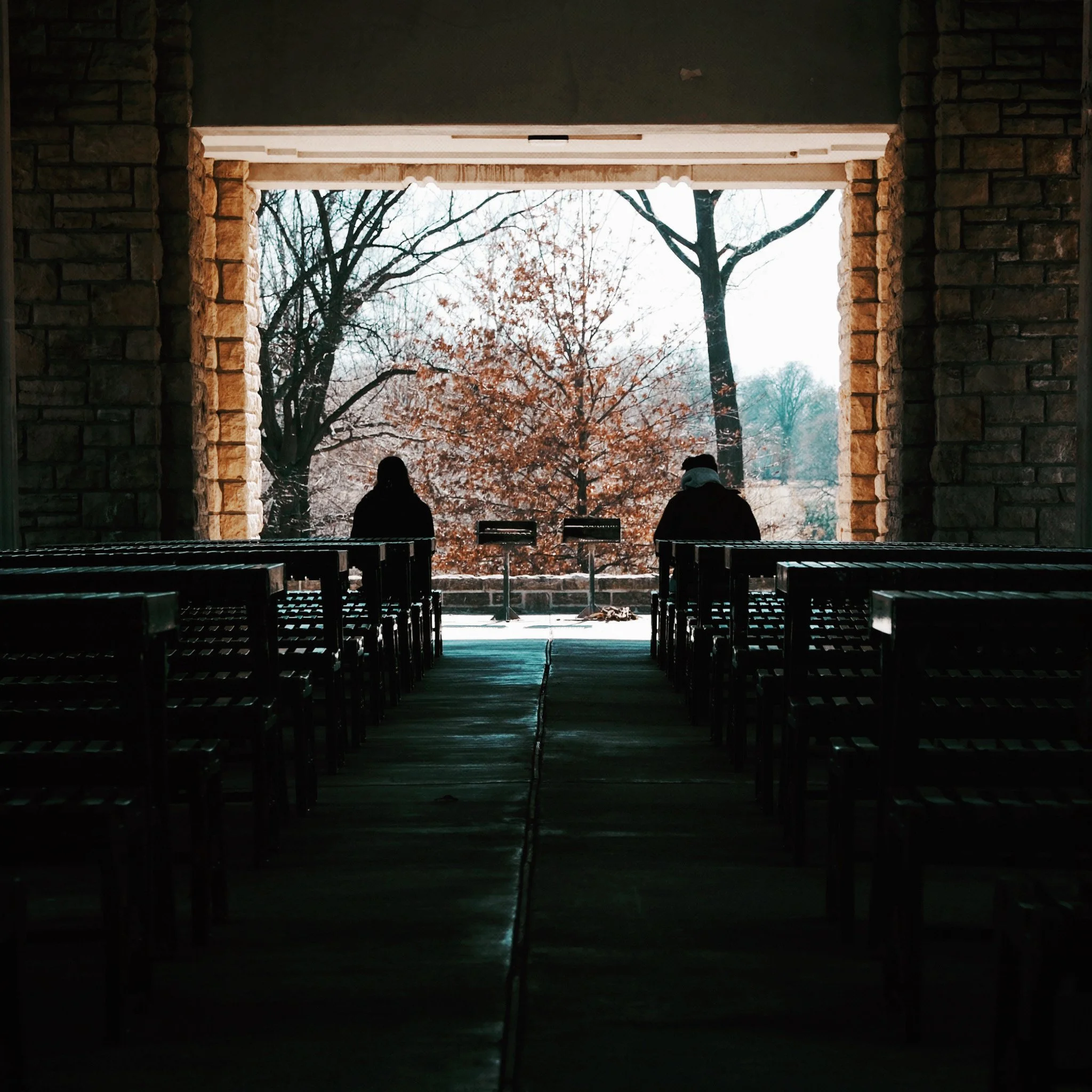 Two people sitting on benches by the window with a view of leafless trees in a winter landscape outside.