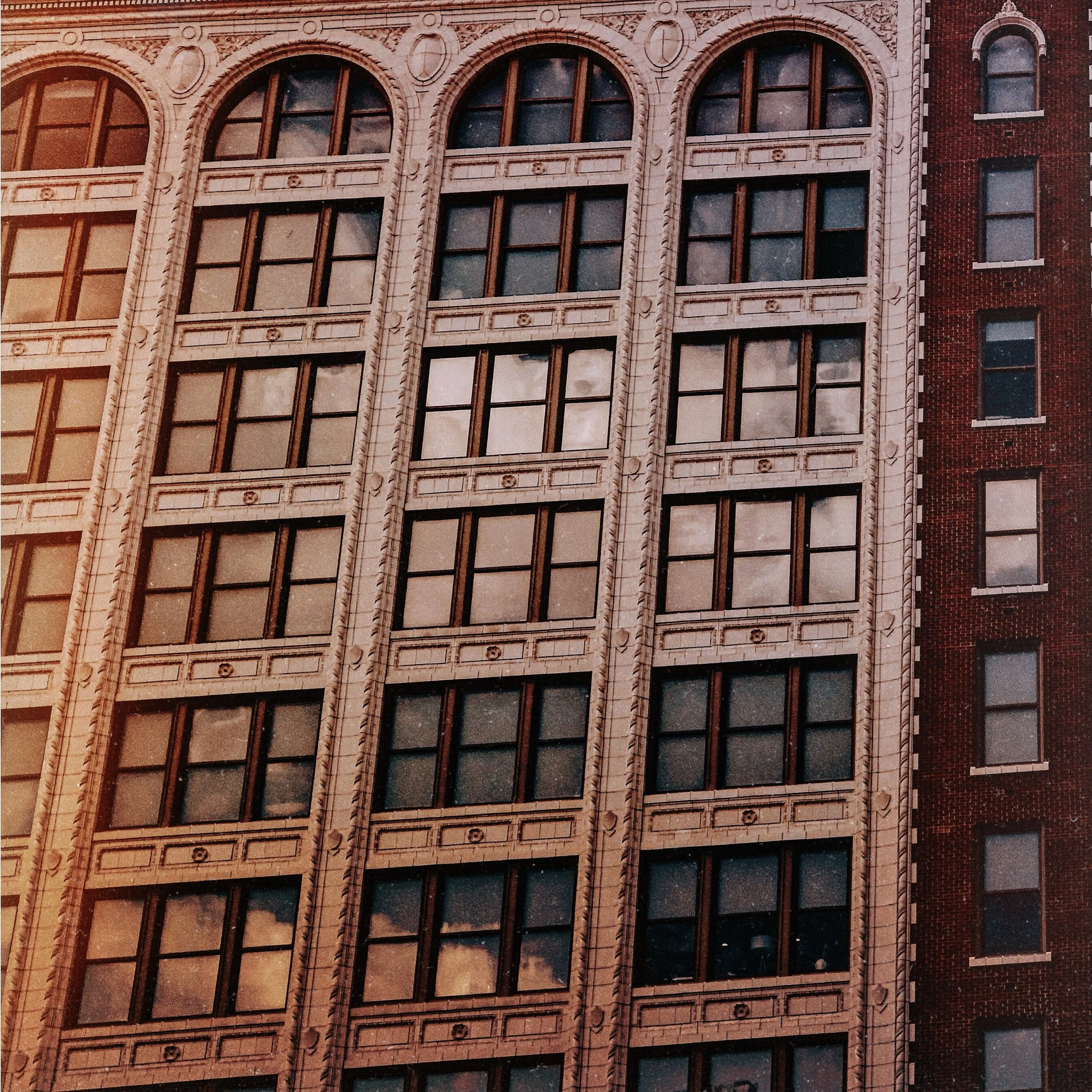 Close-up of a tall building with detailed architectural features around its multiple arched windows, showing a brick exterior on the right side.