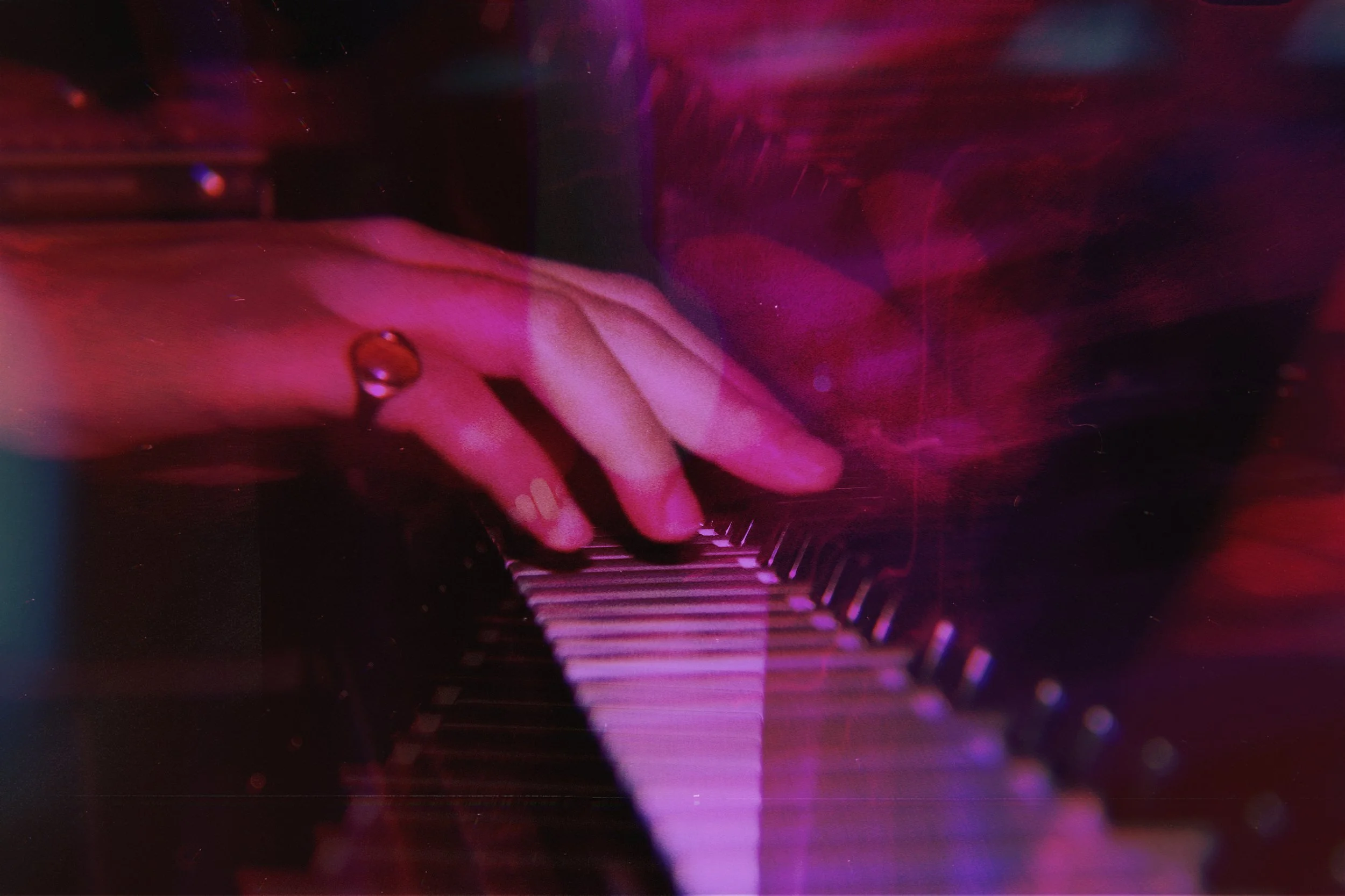 Close-up of a person's hand playing a piano with pink and purple lighting effects.