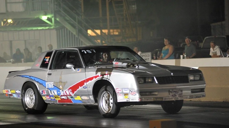 A drag racing car at night with spectators in the background.