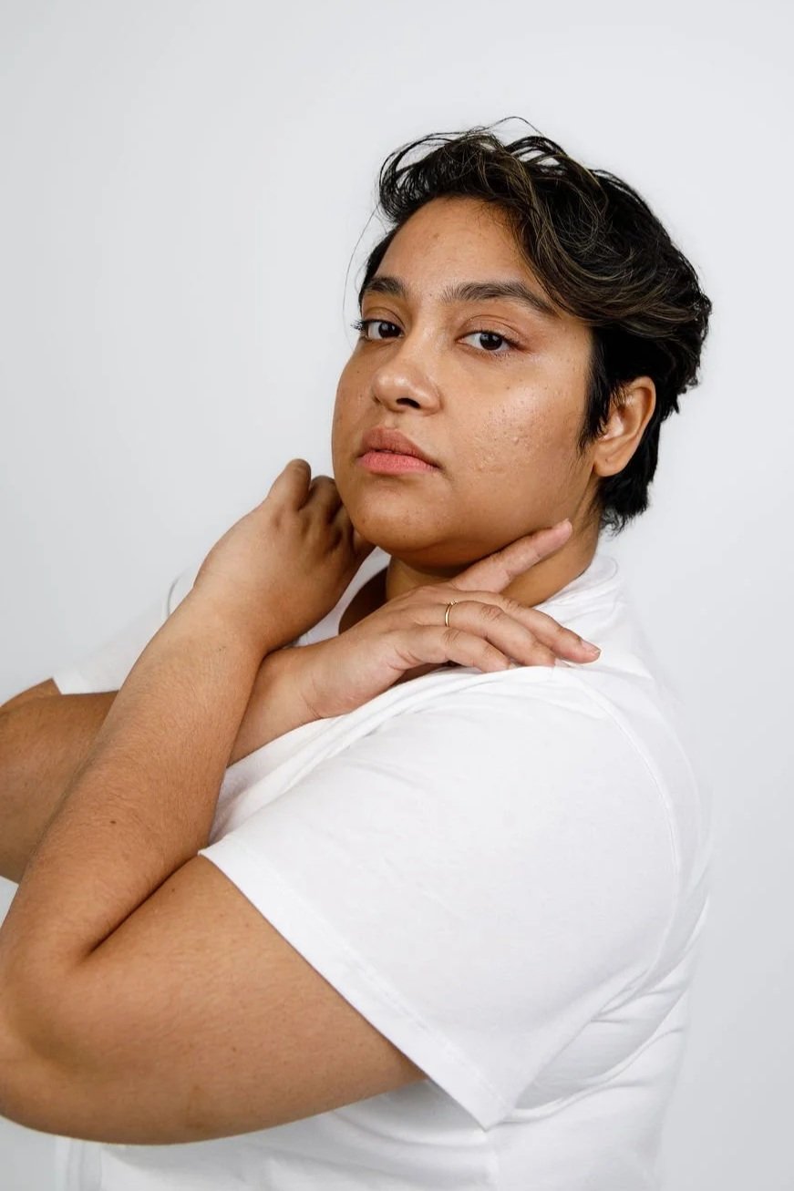 Bengali actor with short, curly, black hair looking into the camera, while their hands frame their face
