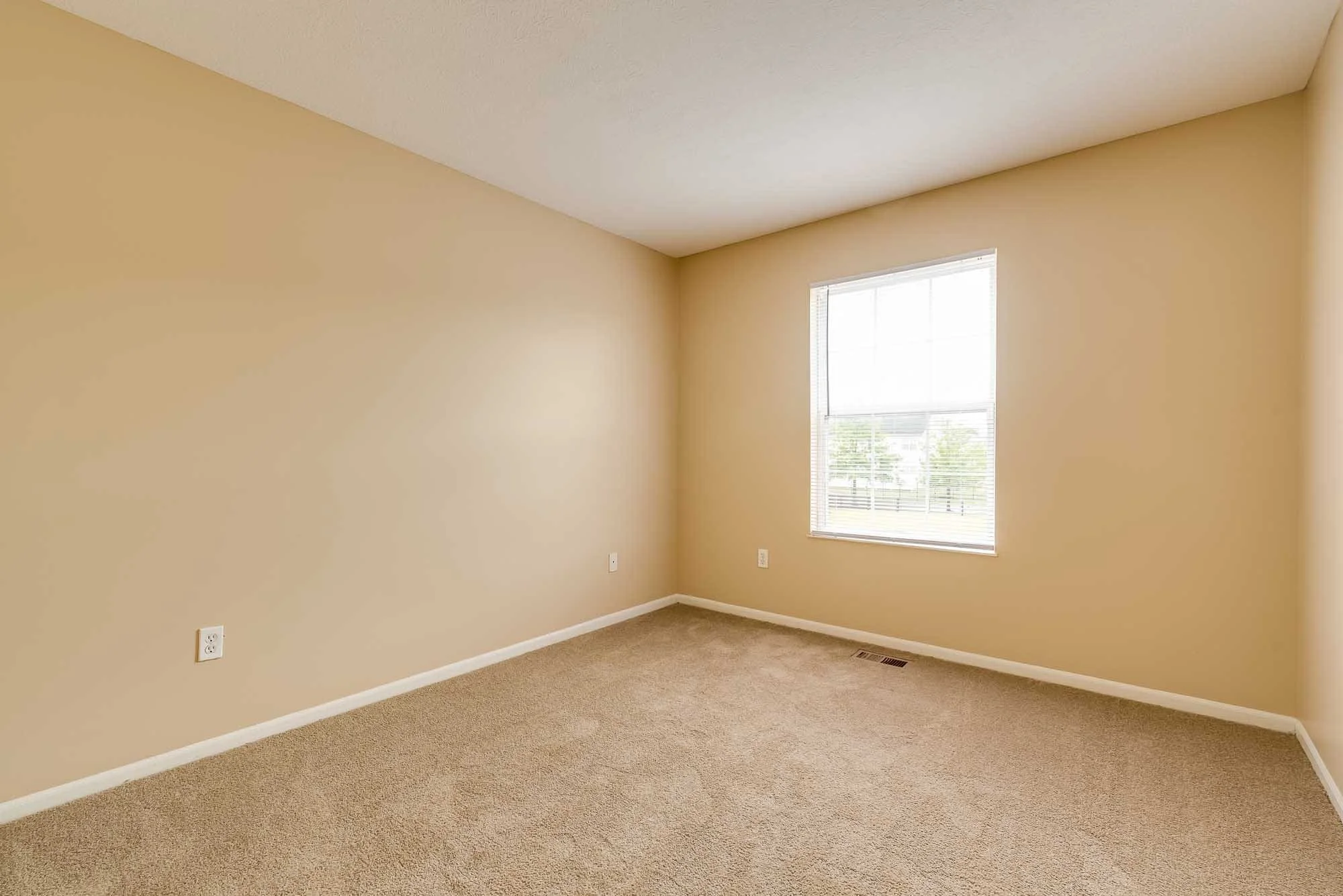 Empty room with beige walls, a window with blinds, beige carpet, and ceiling air vent.