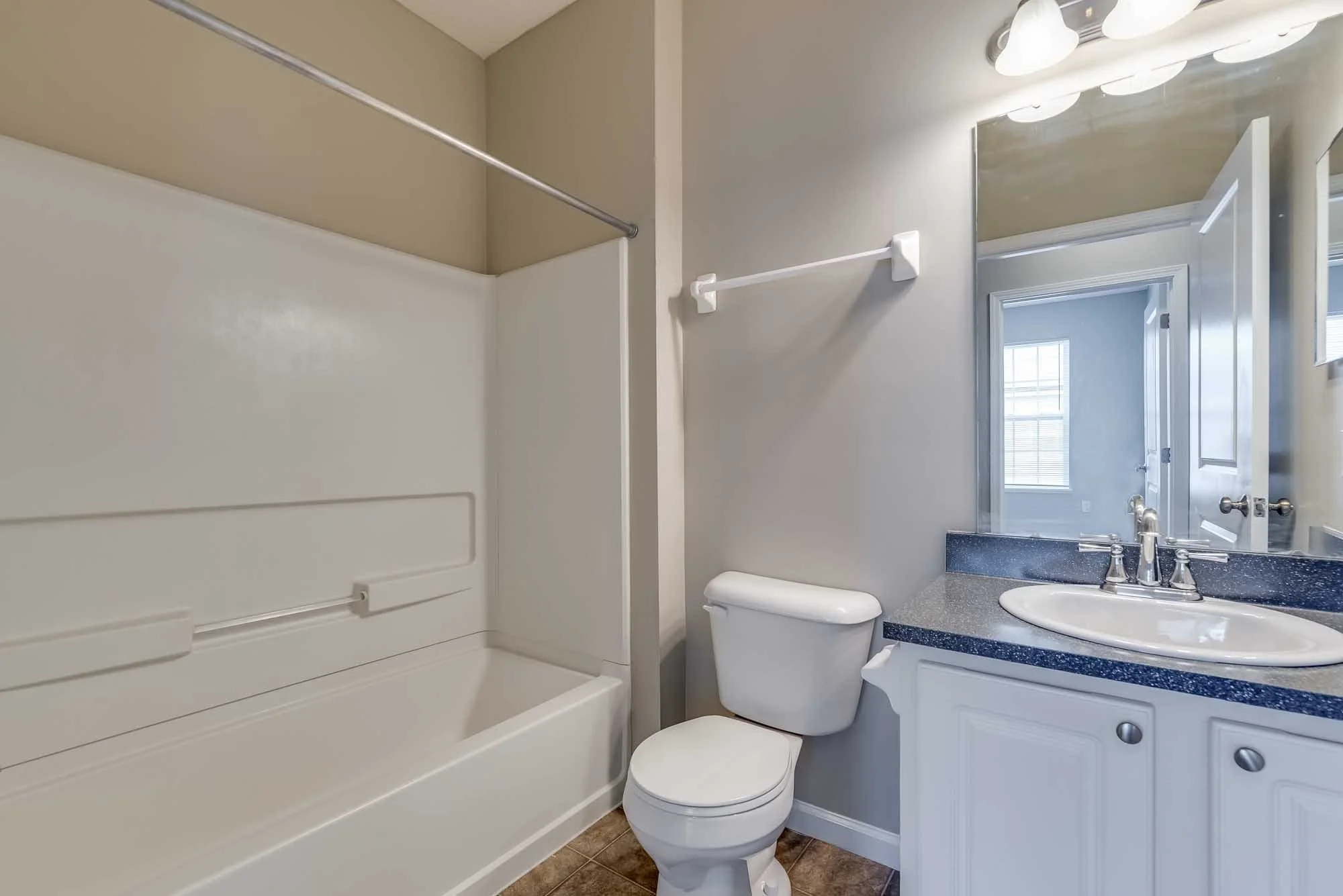 Bathroom with a bathtub/shower, toilet, white vanity with a sink, mirror, and window.