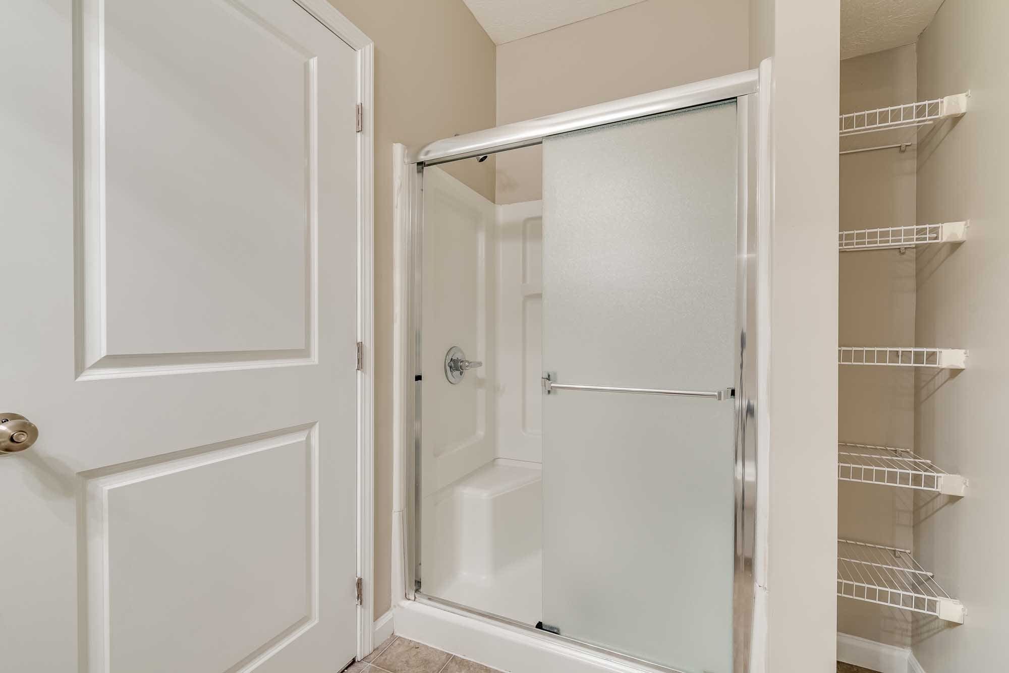 Empty laundry or storage closet with a sliding door, wire shelves on the right, and a small built-in shower or tub with a faucet inside.