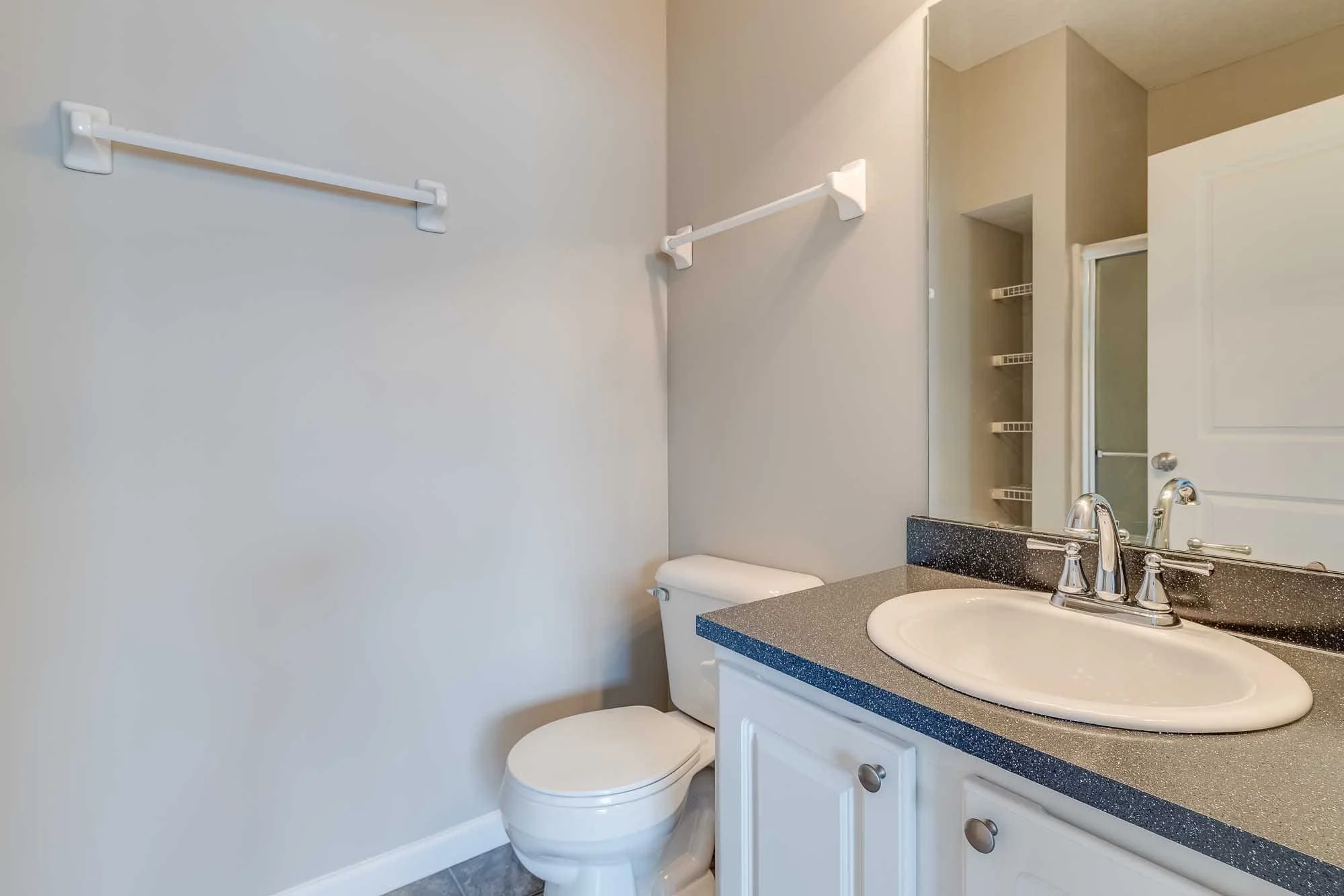 Bathroom with a toilet, a sink with a countertop, a mirror above the sink, and a towel bar on the wall.