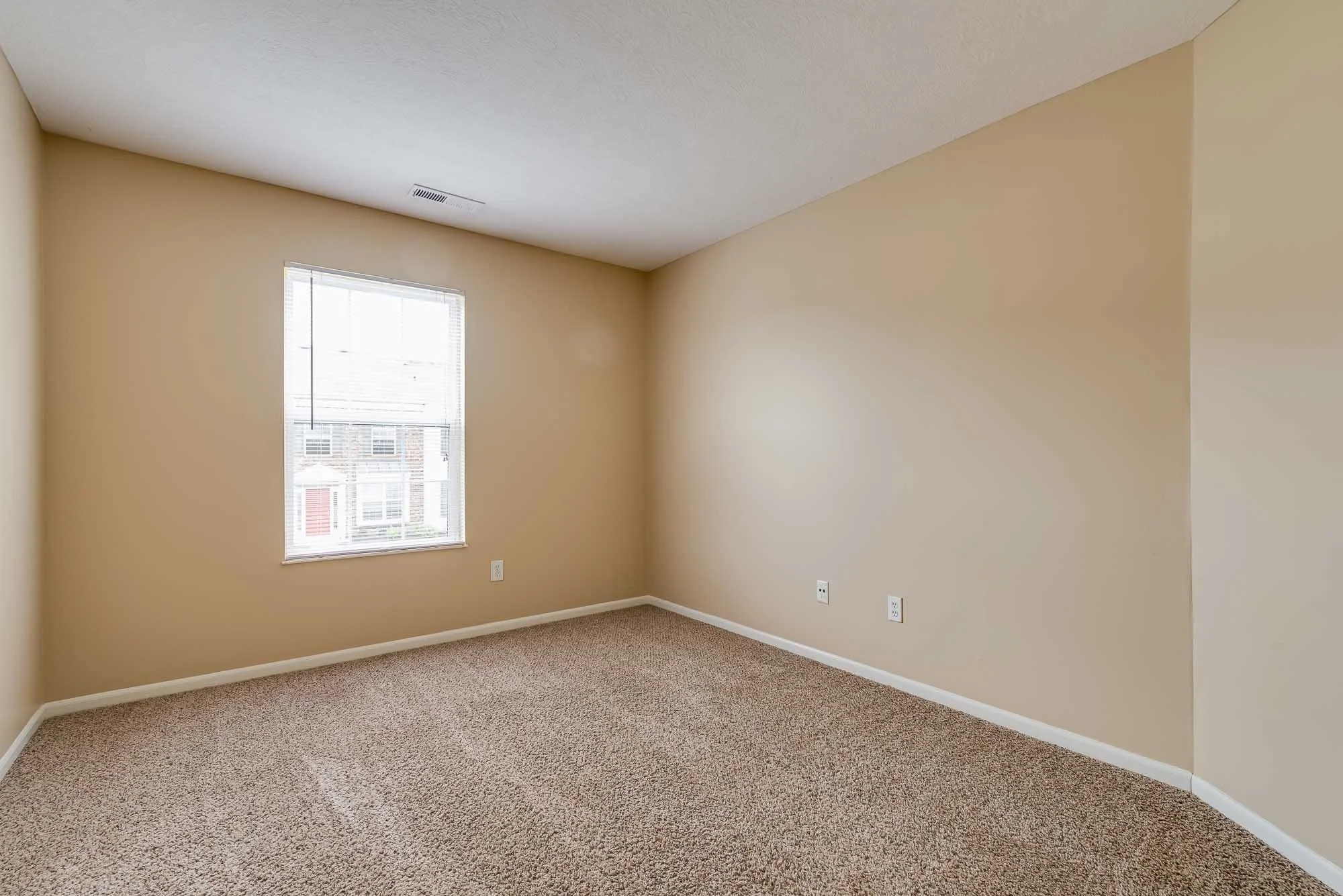 Empty beige room with a window and carpeted floor.