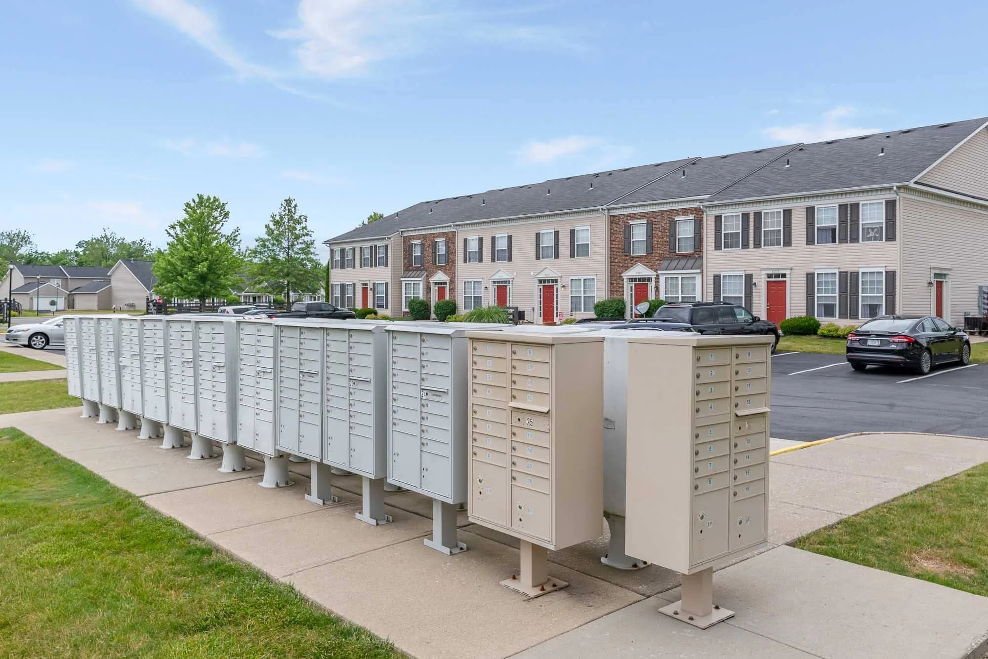 Apartment complex with red doors, parking lot with cars, and mailboxes in the foreground.