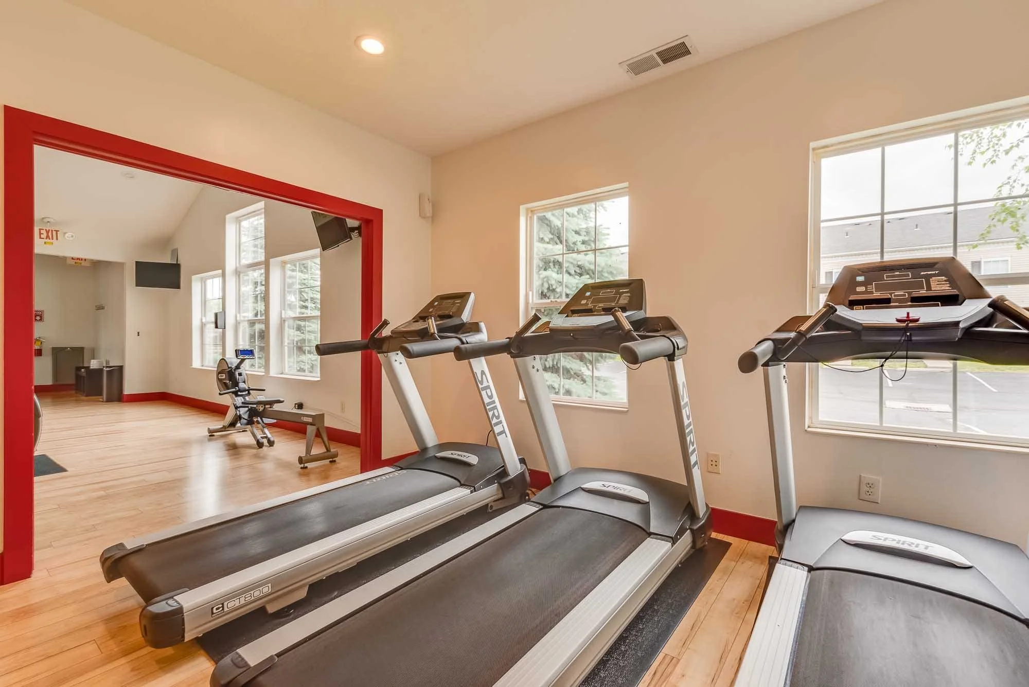 Indoor gym with exercise treadmills facing a wall of windows, displaying a view of outdoor trees.